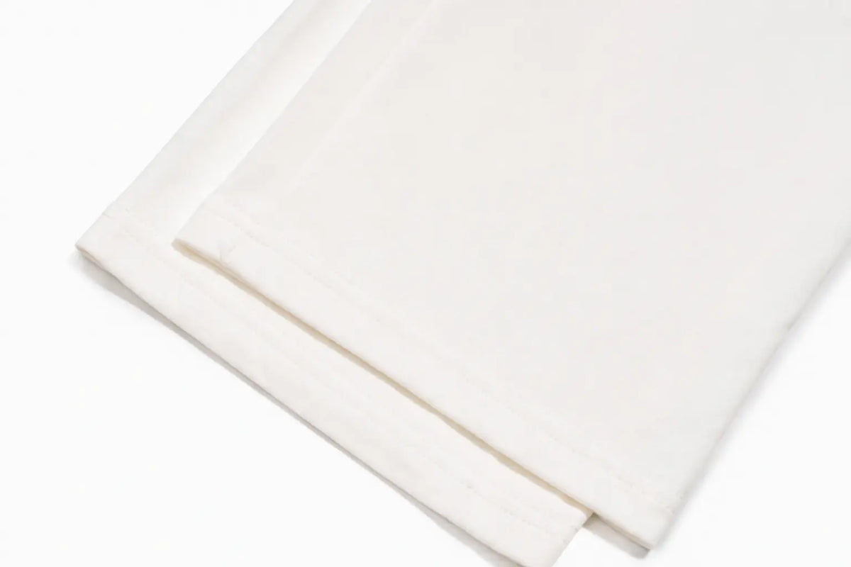 A close-up of folded white fabric, likely a bed sheet or pillowcase, showing a smooth texture and clean stitched border on a white background. TCH Crystal Bear Graphic Wide-Leg Sweatpants