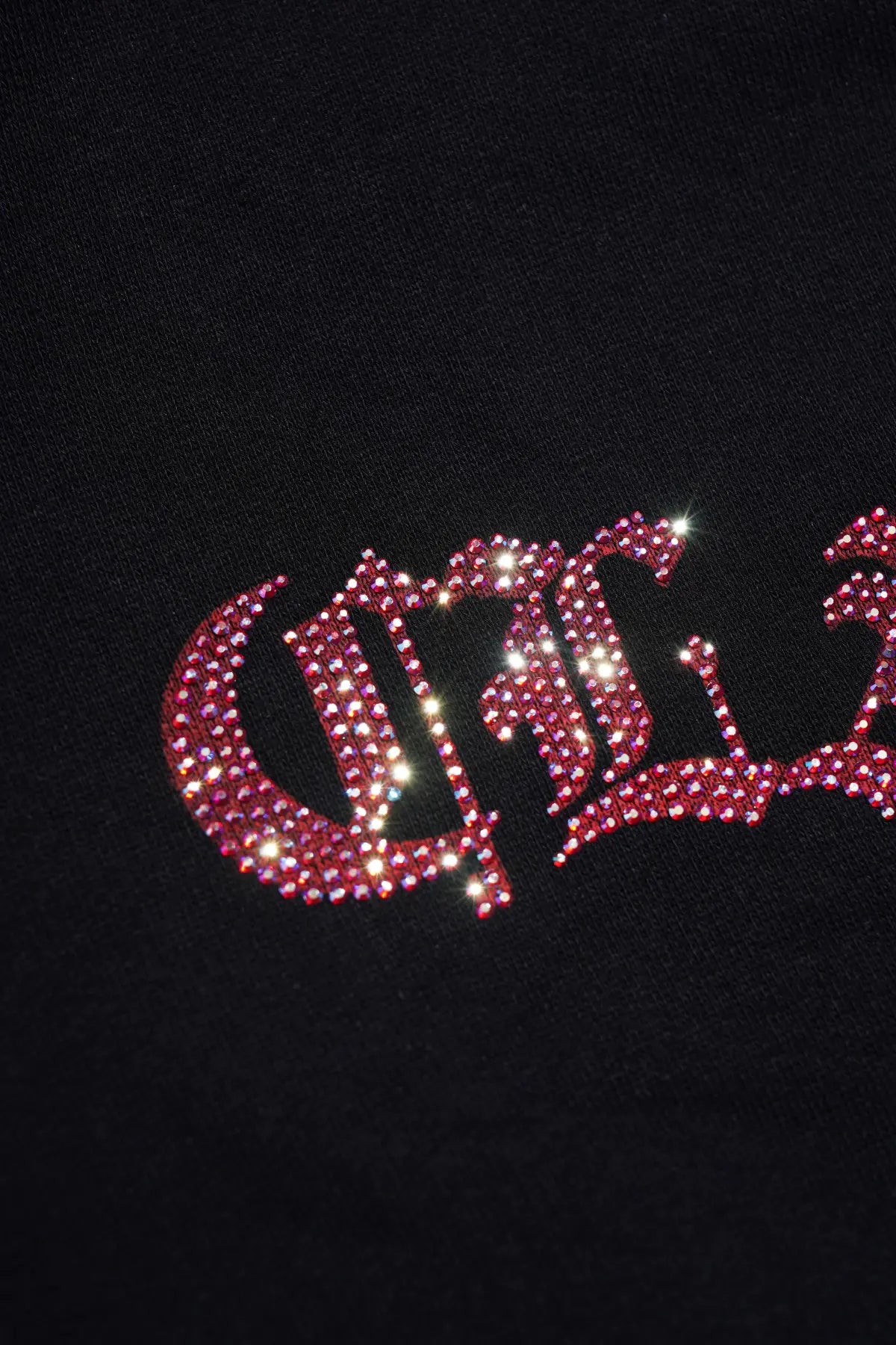 A close-up of a black garment featuring a gothic-style graphic embellished with sparkling red rhinestones. TCH Crystal Eagle Graphic Zip Up Hoodie