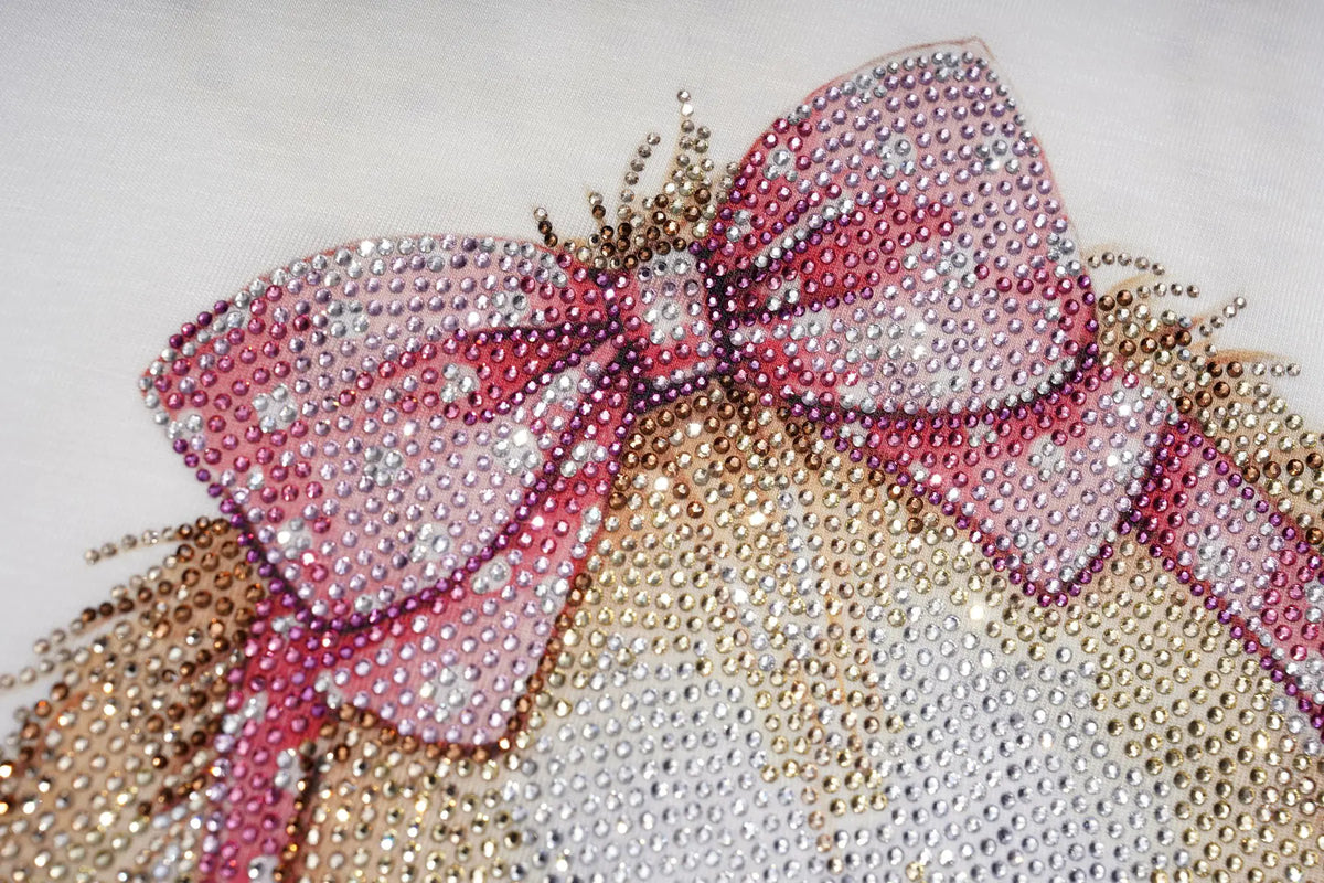 A close-up of a decorative bow embellished with pink and silver rhinestones, attached to a glittering gold and silver embellished surface on a white background. TCH Cute Bunny Rhinestone Graphic Striped Sleeve Long Sleeve T-Shirt