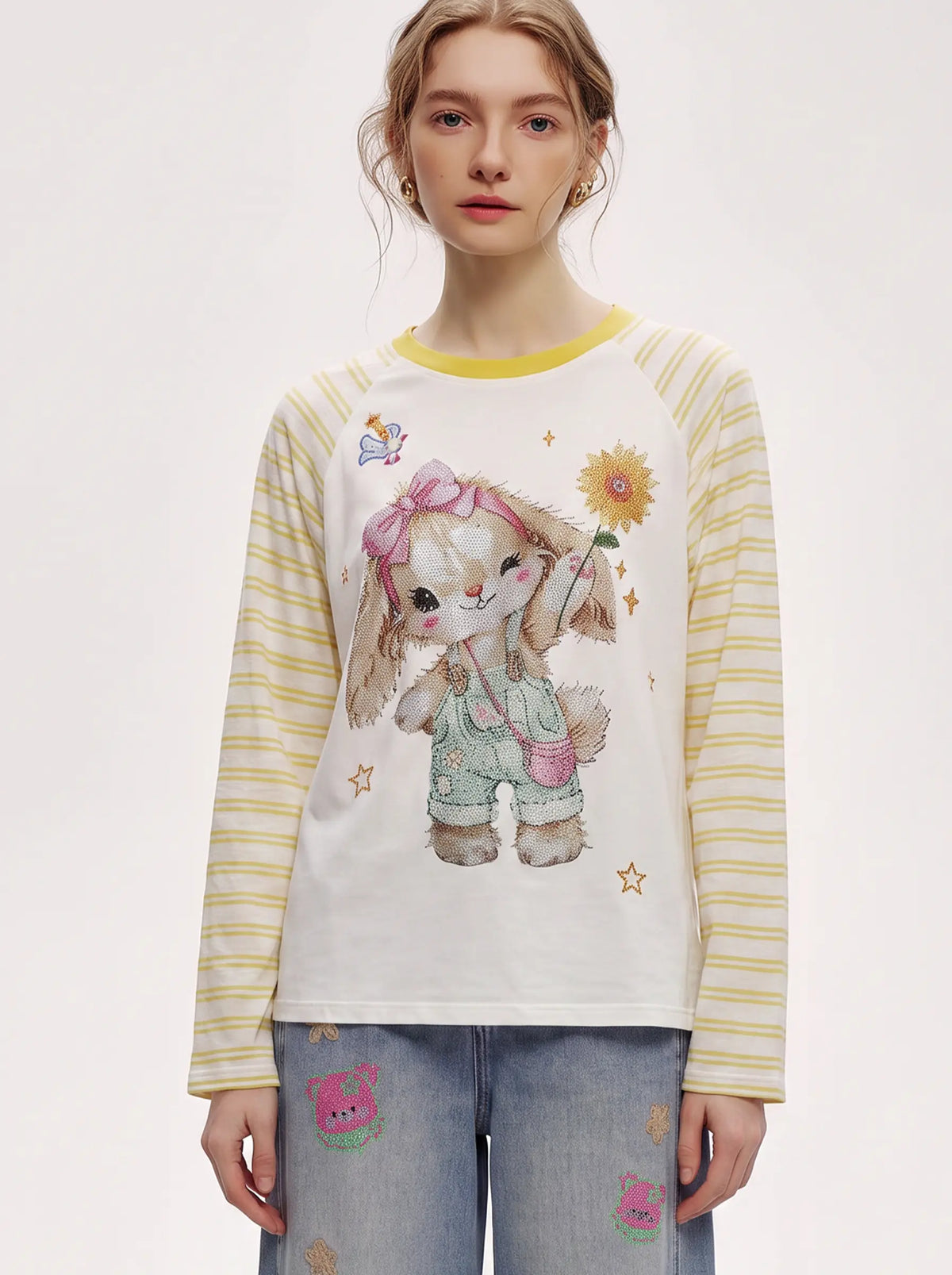 A model wearing a long-sleeve raglan t-shirt with a cute cartoon bunny graphic on the front, yellow and white striped sleeves, and a yellow collar, paired with light blue jeans. TCH Cute Bunny Rhinestone Graphic Striped Sleeve Long Sleeve T-Shirt