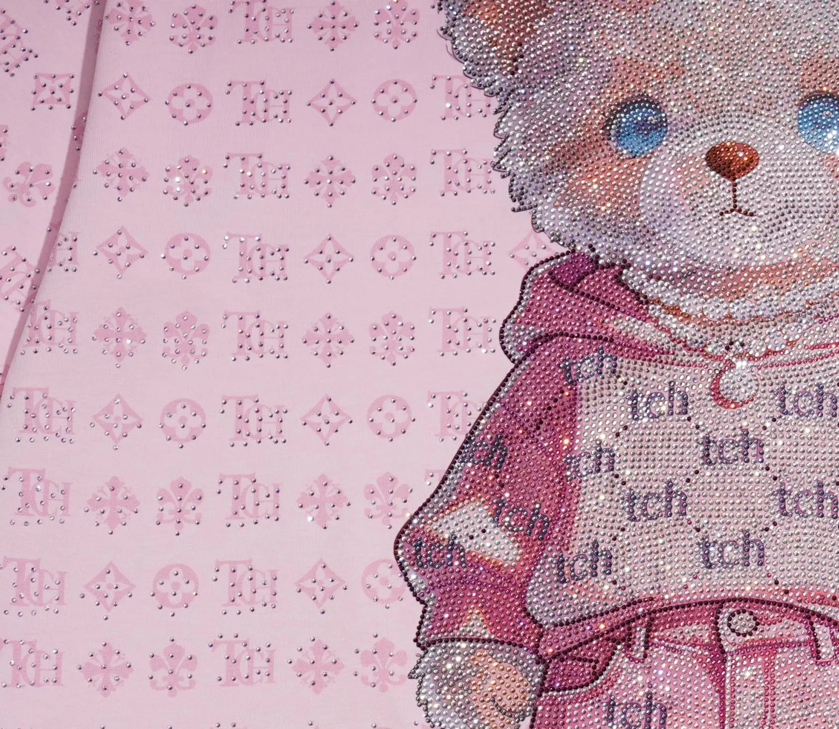 A close-up of a pink fabric featuring a teddy bear illustration and a repeating monogram pattern. The fabric is embellished with rhinestones and sparkly details, and the bear is wearing a pink hoodie with 'tch' lettering. TCH Cute Hoodie Teddy Bear Rhinestone Oversized T-Shirt Dress