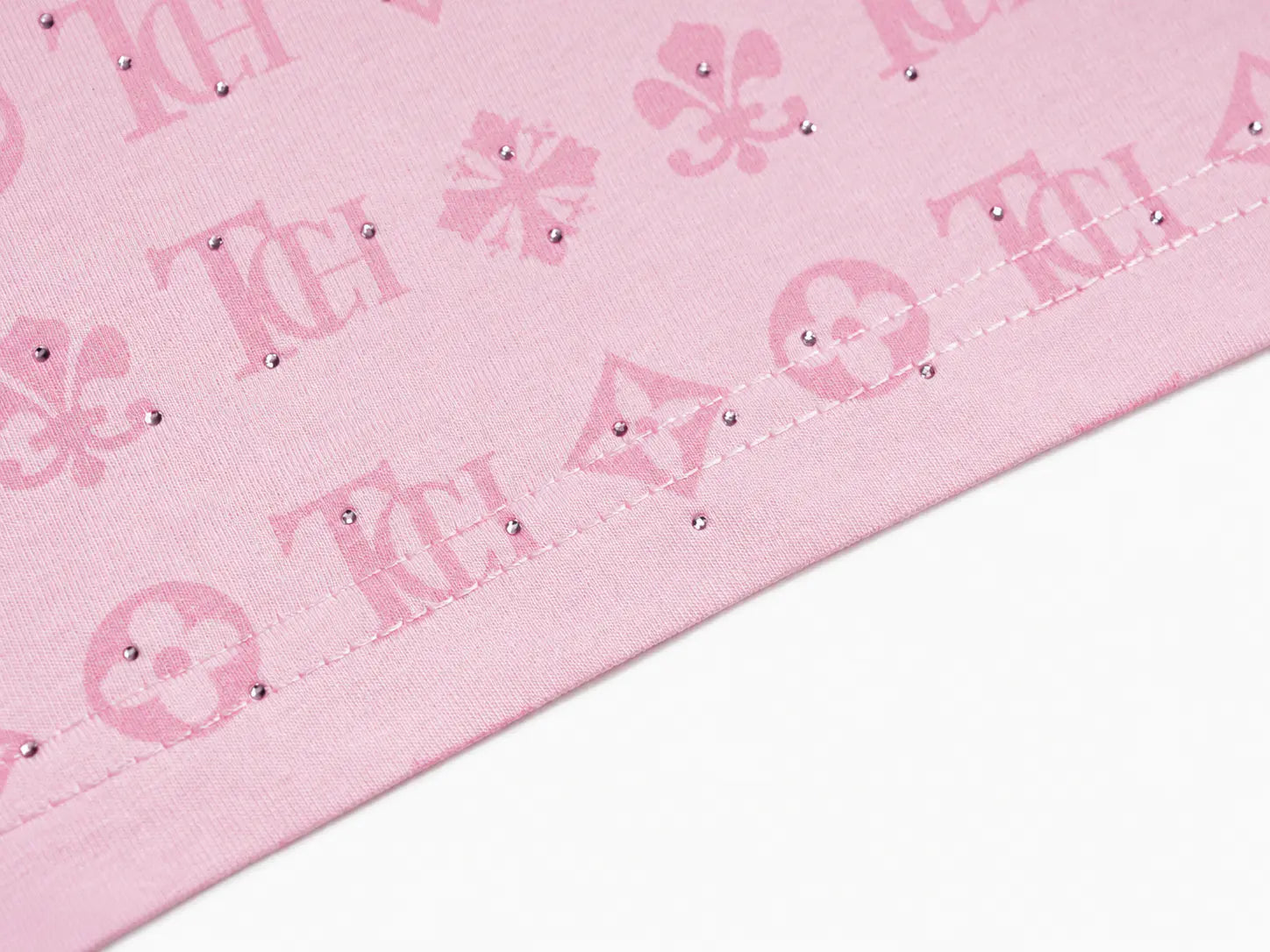 A close-up of a light pink fabric with a repeating monogram-style pattern in darker pink, featuring small rhinestone embellishments along the stitched edge. TCH Cute Hoodie Teddy Bear Rhinestone Oversized T-Shirt Dress