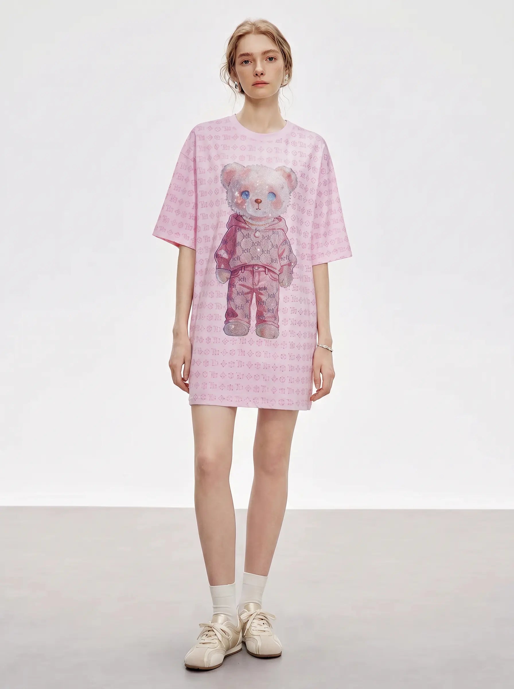 A model stands against a light gray studio background wearing a pink short-sleeve t-shirt dress with a teddy bear graphic on the front, paired with white socks and beige sneakers. TCH Cute Hoodie Teddy Bear Rhinestone Oversized T-Shirt Dress
