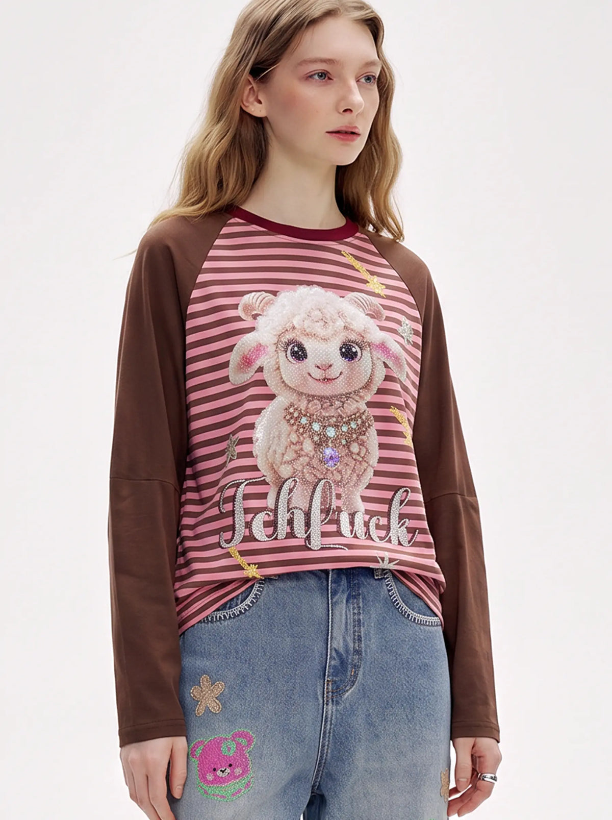 A model wearing a light blue denim jacket with various embroidered patches, including a teddy bear on the left chest and cherries on the sleeve, styled over a white t-shirt and dark pants. TCH Cute Lamb Pink Striped Raglan Long Sleeve Top