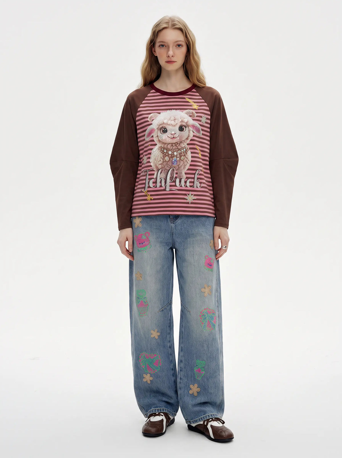 A model stands against a plain white studio background wearing a long-sleeve raglan top with a red-and-white striped body, dark brown sleeves, and a large lamb graphic with the word 'kiffkiff' on the chest, paired with wide-leg blue jeans decorated with small colorful embroidered motifs. TCH Cute Lamb Pink Striped Raglan Long Sleeve Top