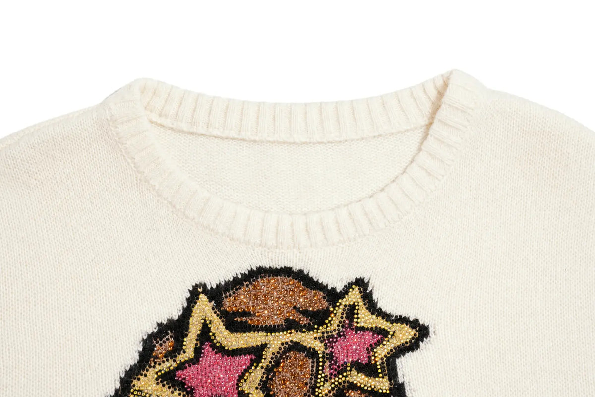 Close-up of a cream-colored knit sweater featuring a decorative graphic with pink star details and gold glitter-like accents on the chest. TCH Cute Puppy Star Graphic Knit Sweater