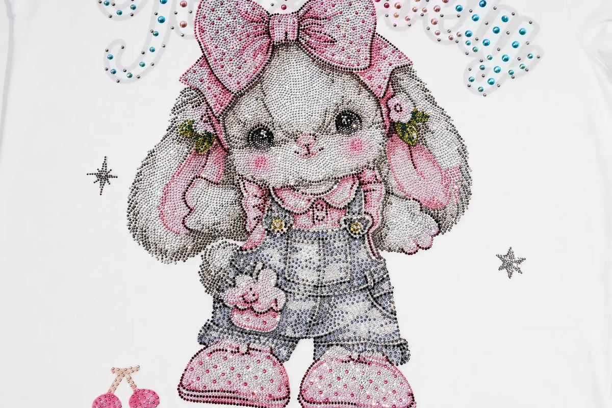 A close-up of a white garment featuring a large, detailed graphic of a cute bunny character adorned with a pink bow, pink polka-dot overalls, and pink boots, embellished with rhinestones. TCH Cute Rhinestone Cat Graphic Pink Long Sleeve T-Shirt