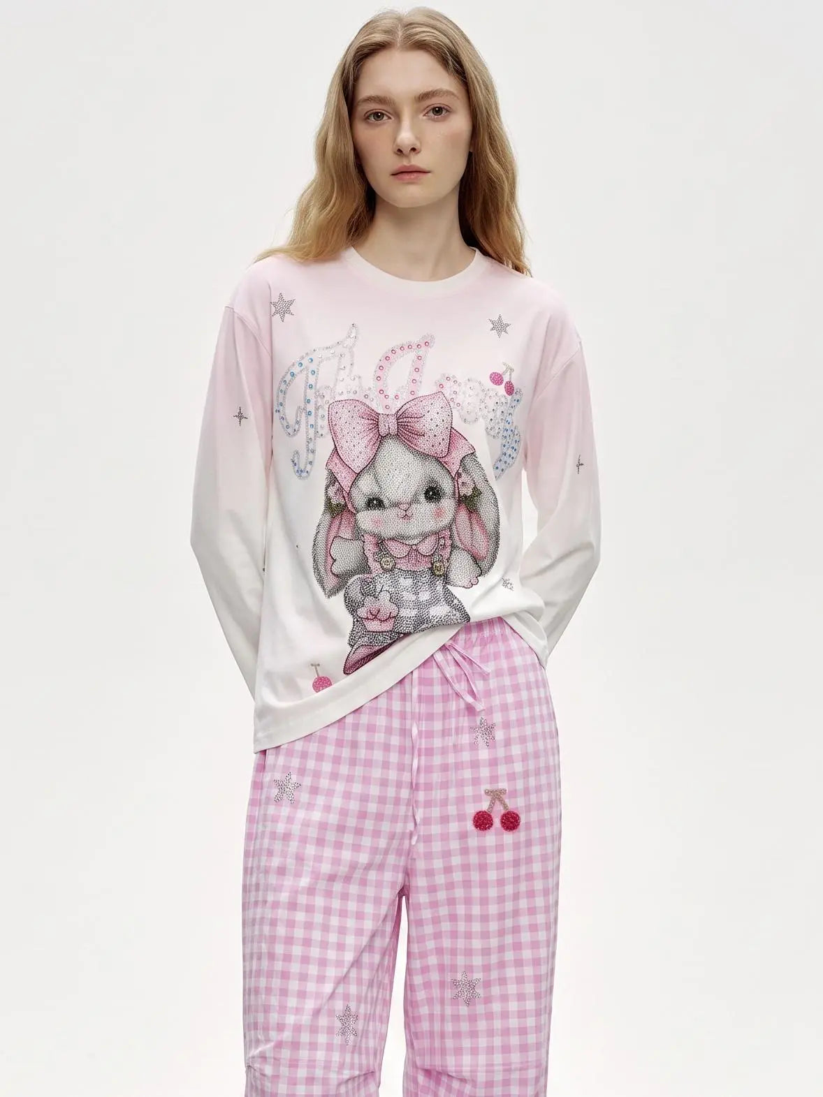A model wearing a light pink and white long-sleeve pajama top with a cute bunny graphic, paired with pink gingham pajama pants with cherry details, against a plain white studio background. TCH Cute Rhinestone Cat Graphic Pink Long Sleeve T-Shirt