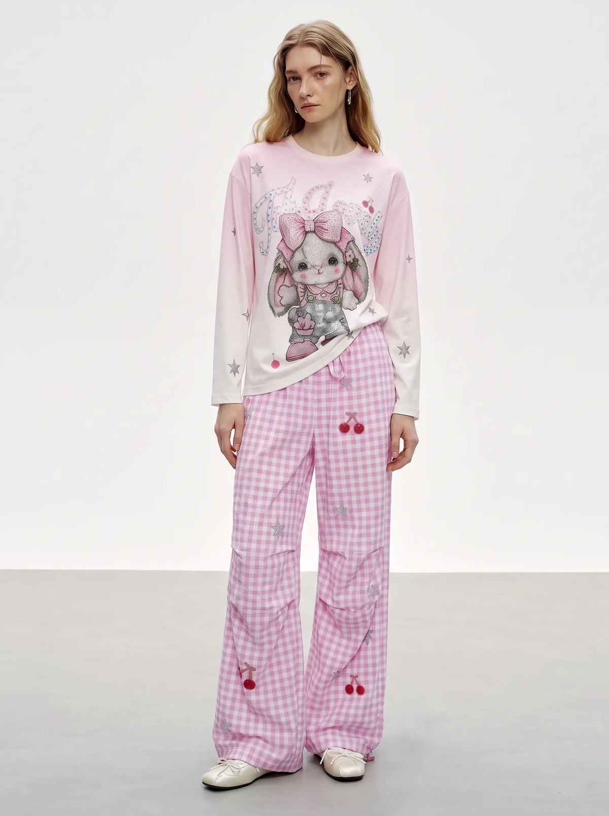 A model wearing a pink and white bunny-themed pajama set, featuring a long-sleeve top with a cartoon bunny graphic and matching gingham pants with cherry prints, set against a plain studio background. TCH Cute Rhinestone Cat Graphic Pink Long Sleeve T-Shirt