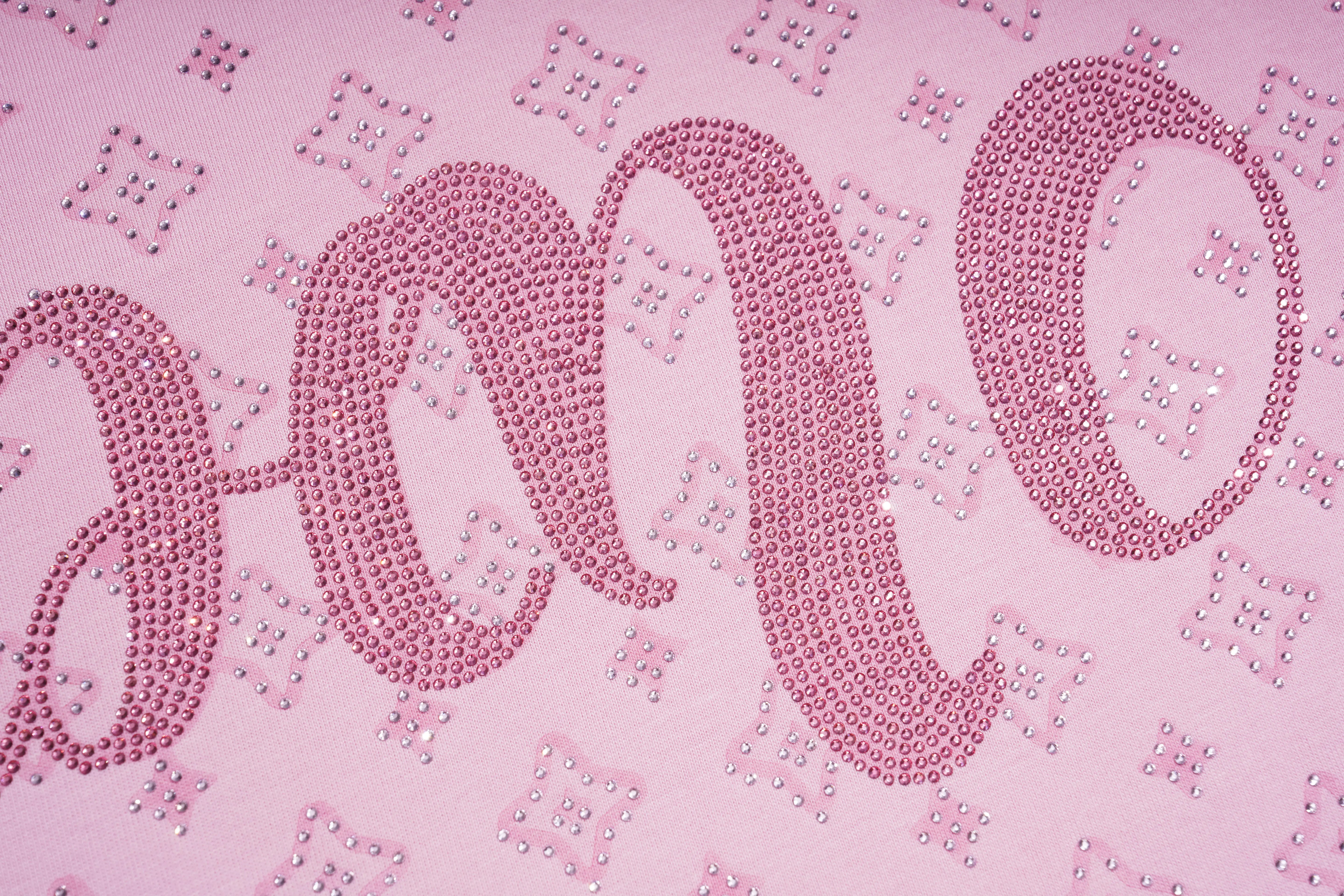 A close-up of a light pink fabric featuring a large cursive word outlined with pink rhinestones, with smaller matching rhinestone motifs scattered across the background. TCH Cute Teddy Bear Rhinestone Oversized T-Shirt Dress