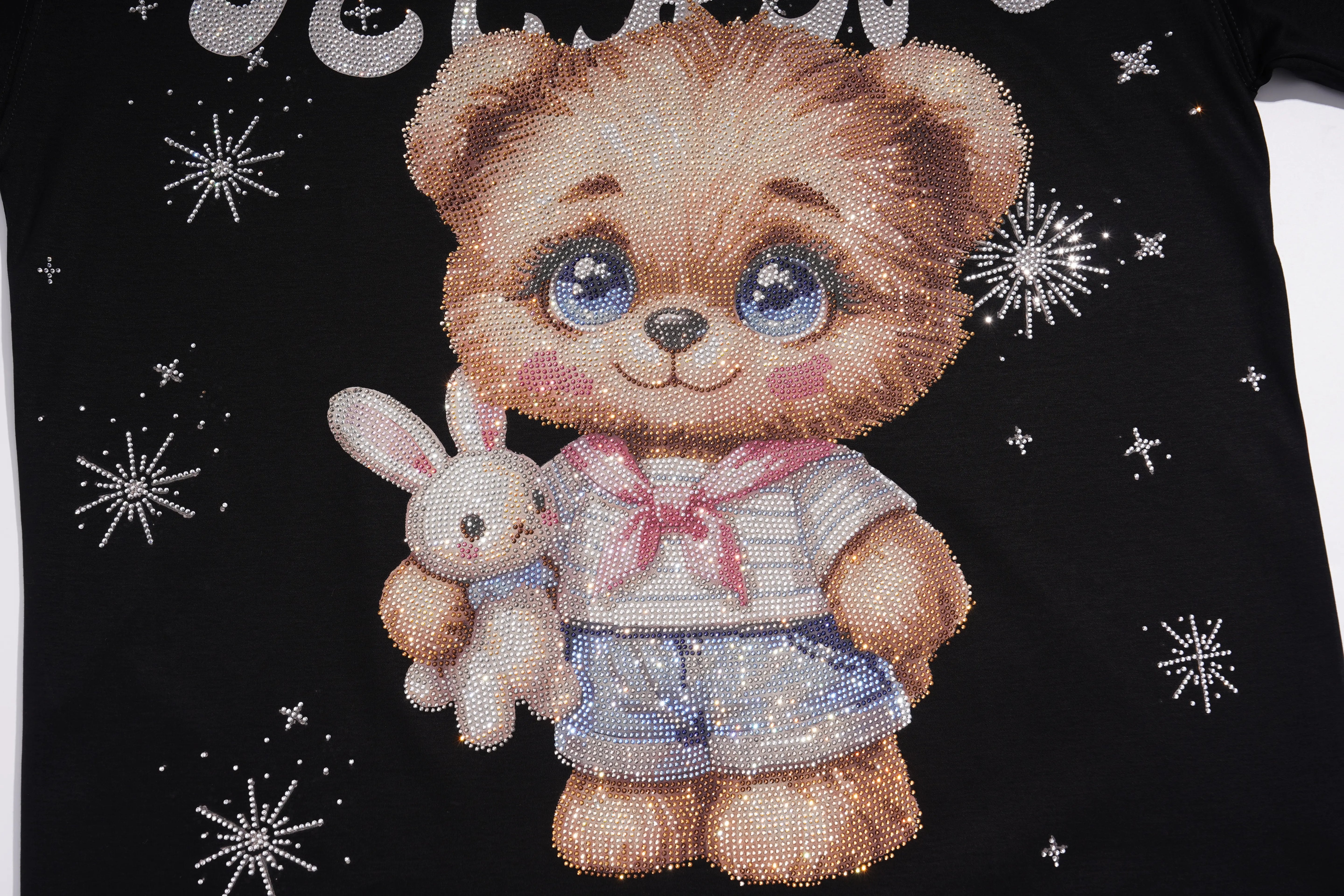 A close-up of a black garment featuring a large teddy bear graphic with blue eyes, holding a small bunny, with silver snowflake embellishments on a black background. TCH Cute Teddy Bear Rhinestone Oversized T-Shirt Dress