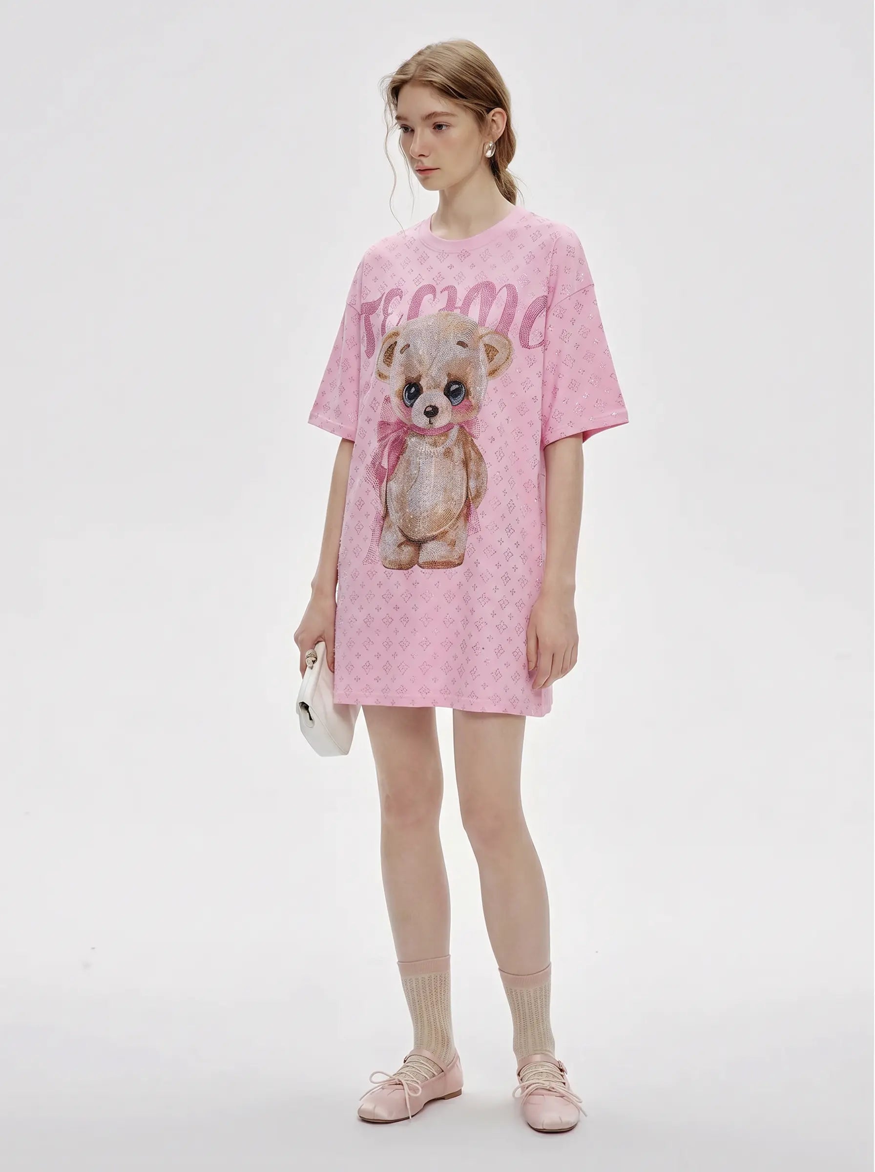 A model stands against a light gray studio background wearing a pink short-sleeve T-shirt dress with a teddy bear graphic and pink script text across the chest. TCH Cute Teddy Bear Rhinestone Oversized T-Shirt Dress
