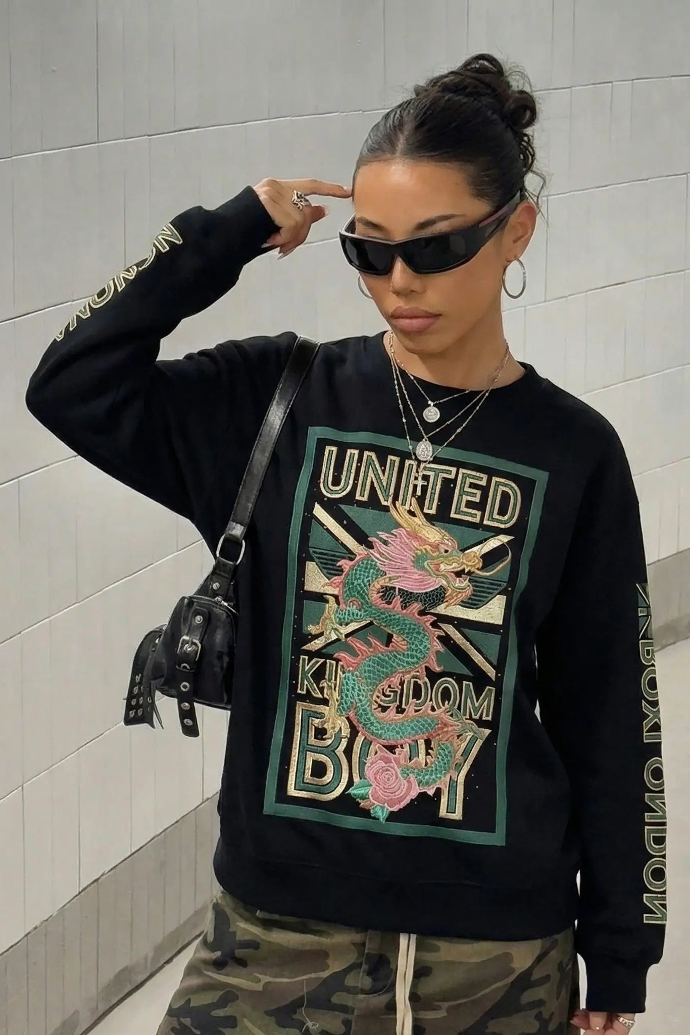 Person wearing a black sweatshirt with a colorful graphic design and text, standing against a light gray wall. TCH Dragon Embroidered Rhinestone Sweatshirt-