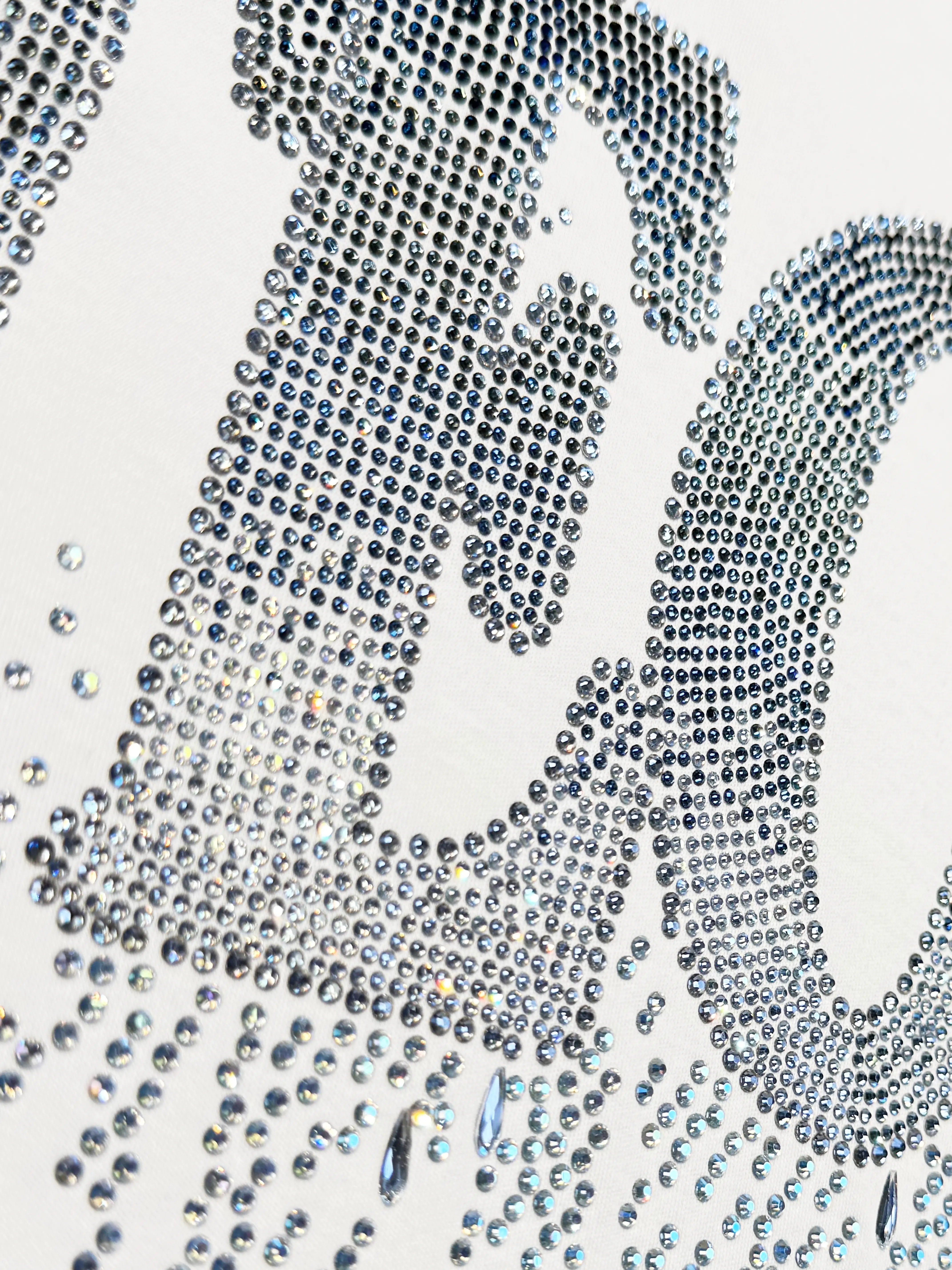 A close-up of a rhinestone-covered letterform on a white background, featuring dense rows of small clear and silver-toned stones with some scattered loose stones below. TCH Dripping Rhinestone Logo Graphic T-Shirt