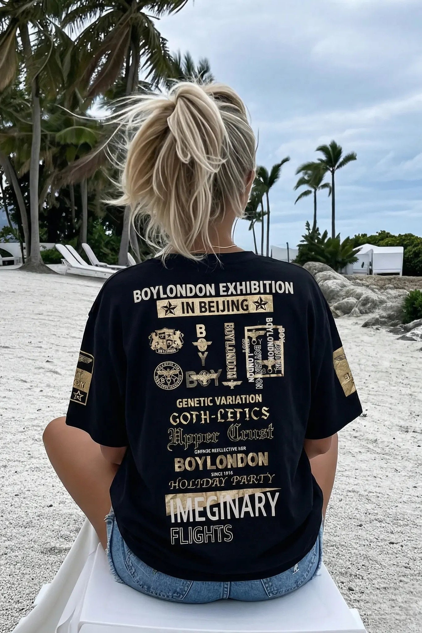 Person wearing a black t-shirt with text and graphics, sitting on a beach. TCH Embroidered Floral Butterfly Rhinestone T-Shirt