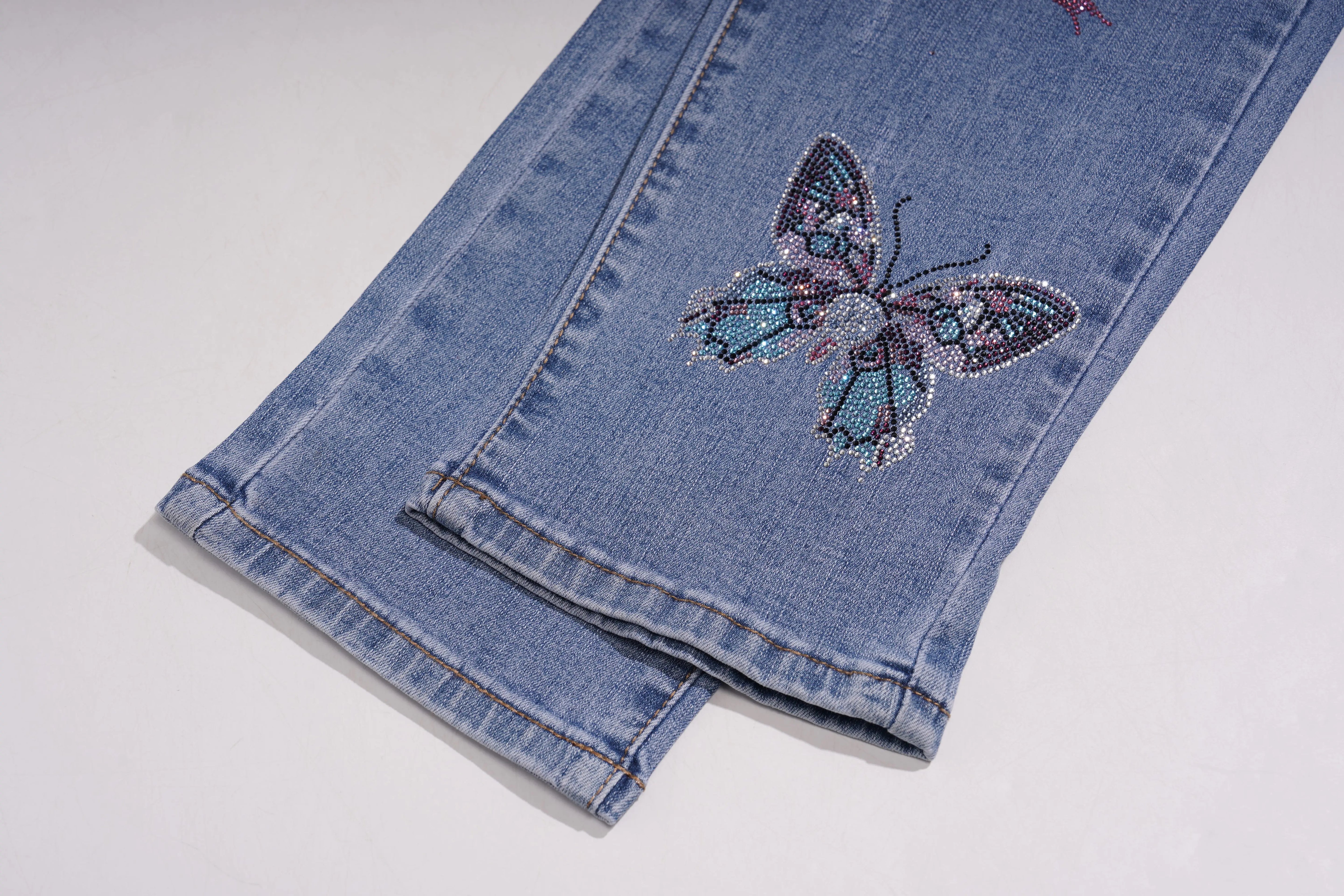 Folded blue jeans with a decorative butterfly on a white background, TCH Embroidered Rose & Rhinestone Butterfly Denim Jeans