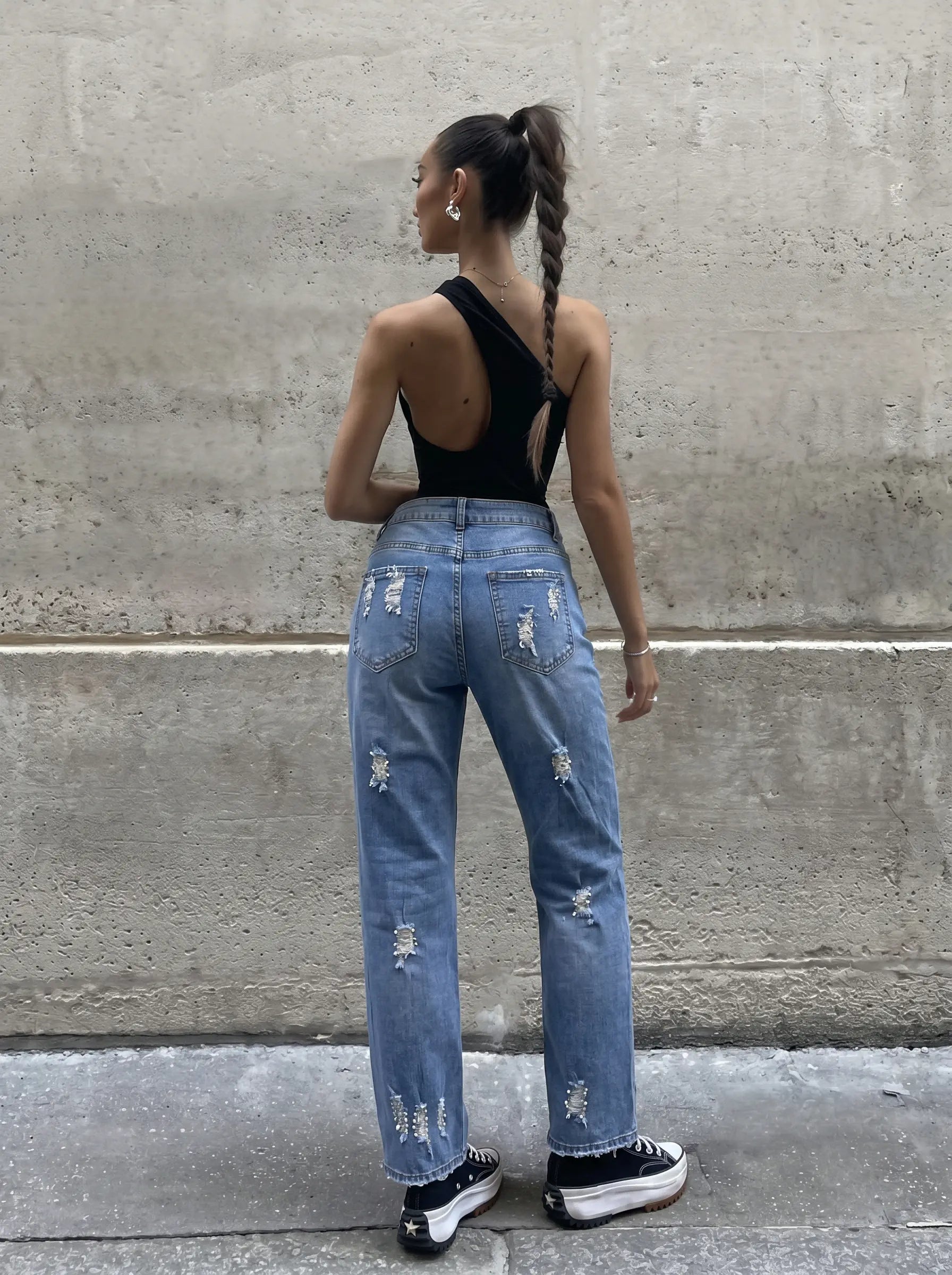 Person wearing blue distressed jeans and black sneakers standing against a concrete wall. TCH Embroidered Rose & Rhinestone Butterfly Denim Jeans