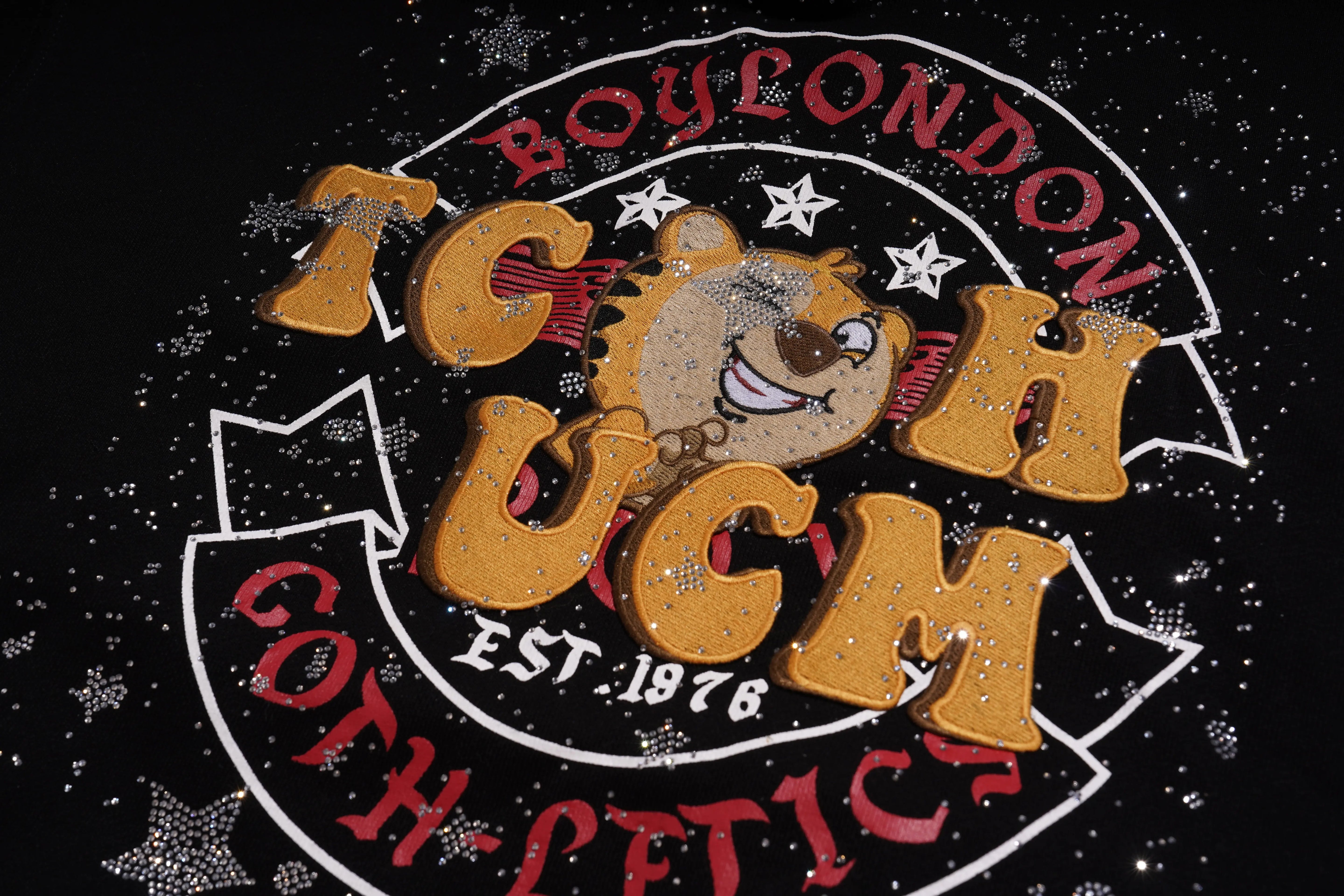 Decorative logo with text and a bear illustration on a black background, TCH Embroidered TCHUCM Rhinestone Hoodie