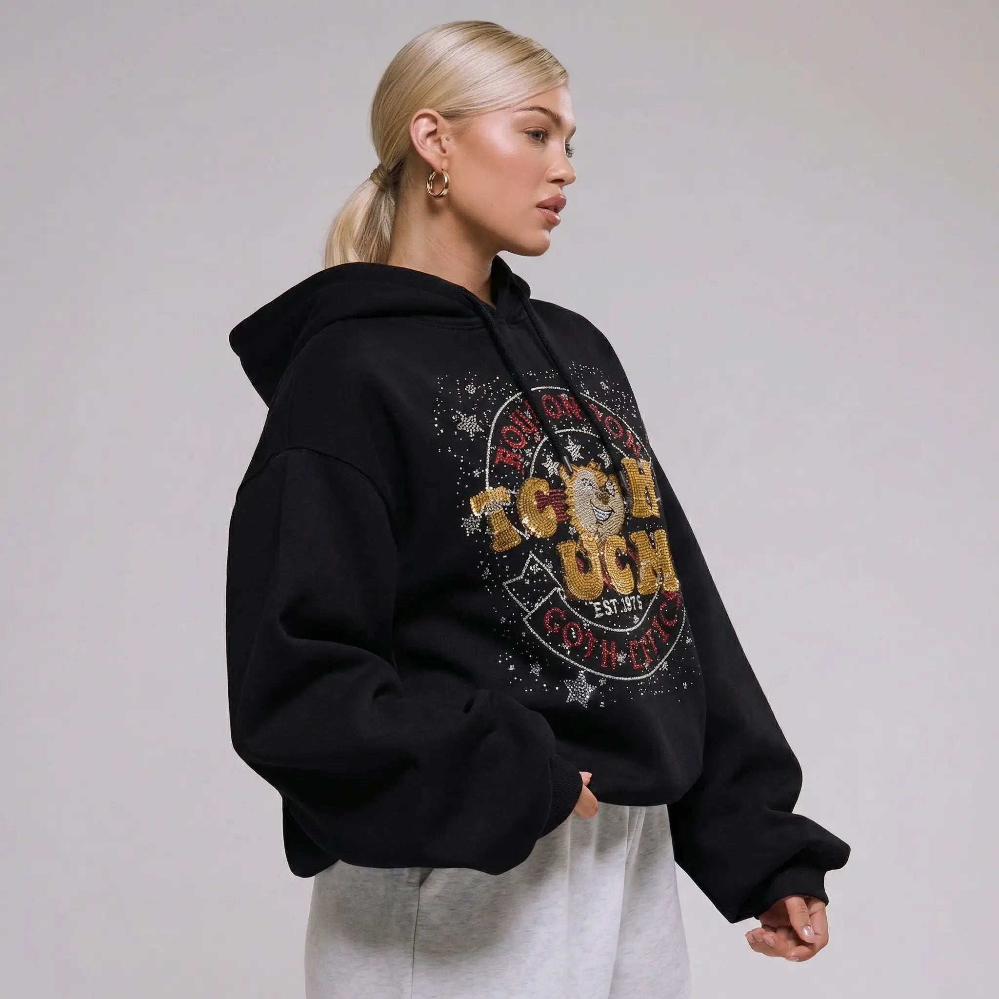 Person wearing a black hoodie with a colorful graphic design on a plain background, TCH Embroidered TCHUCM Rhinestone Hoodie