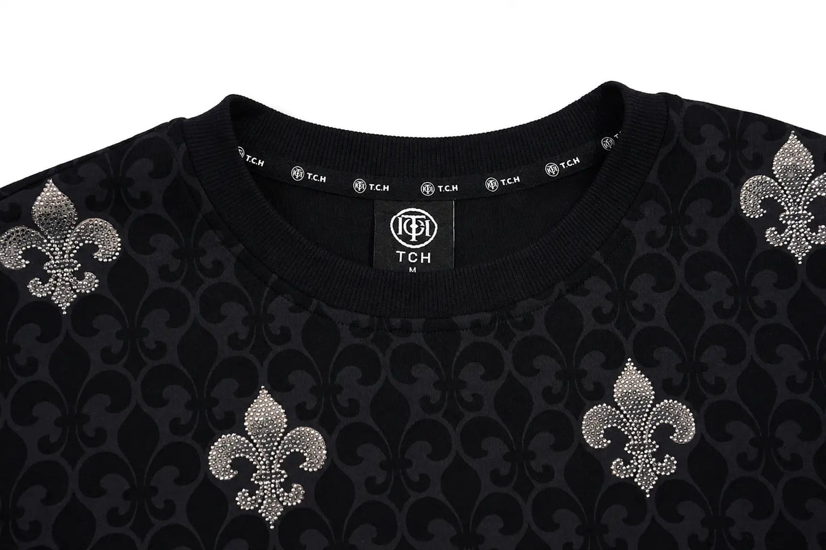 Close-up of a black crewneck sweater featuring a dark damask pattern and three silver rhinestone-embellished fleur-de-lis motifs on the front. TCH Fleur-de-Lis Pattern Layered Long Sleeve T-Shirt