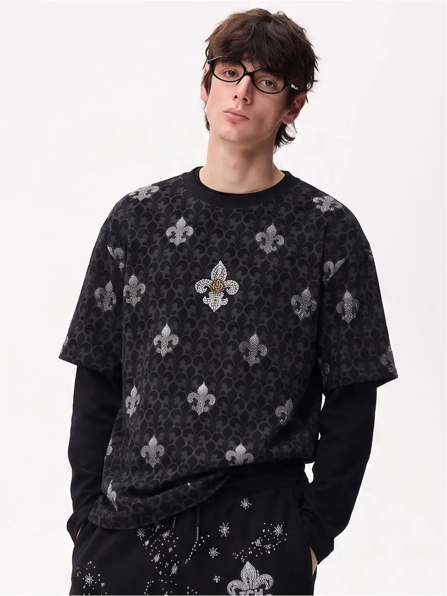 A model wearing a black crewneck sweatshirt with a repeating silver fleur-de-lis pattern and a central embellished crest, layered over a black long-sleeve shirt, against a plain white background. TCH Fleur-de-Lis Pattern Layered Long Sleeve T-Shirt