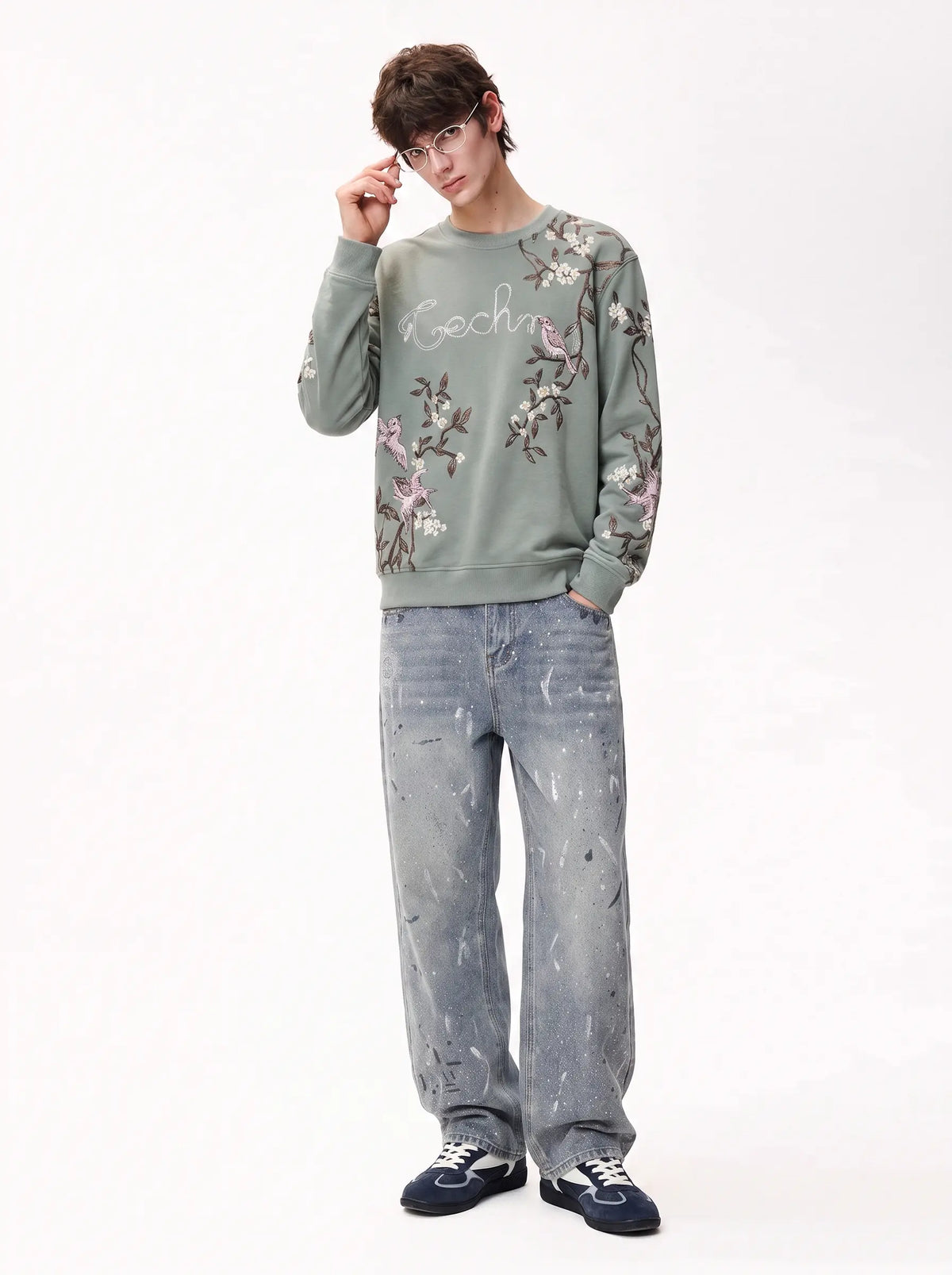 A model wearing a sage green embroidered sweatshirt with floral details, paired with light-wash jeans and dark sneakers, standing against a plain white studio background. TCH Floral Bird Embroidery Oversized Sweatshirt
