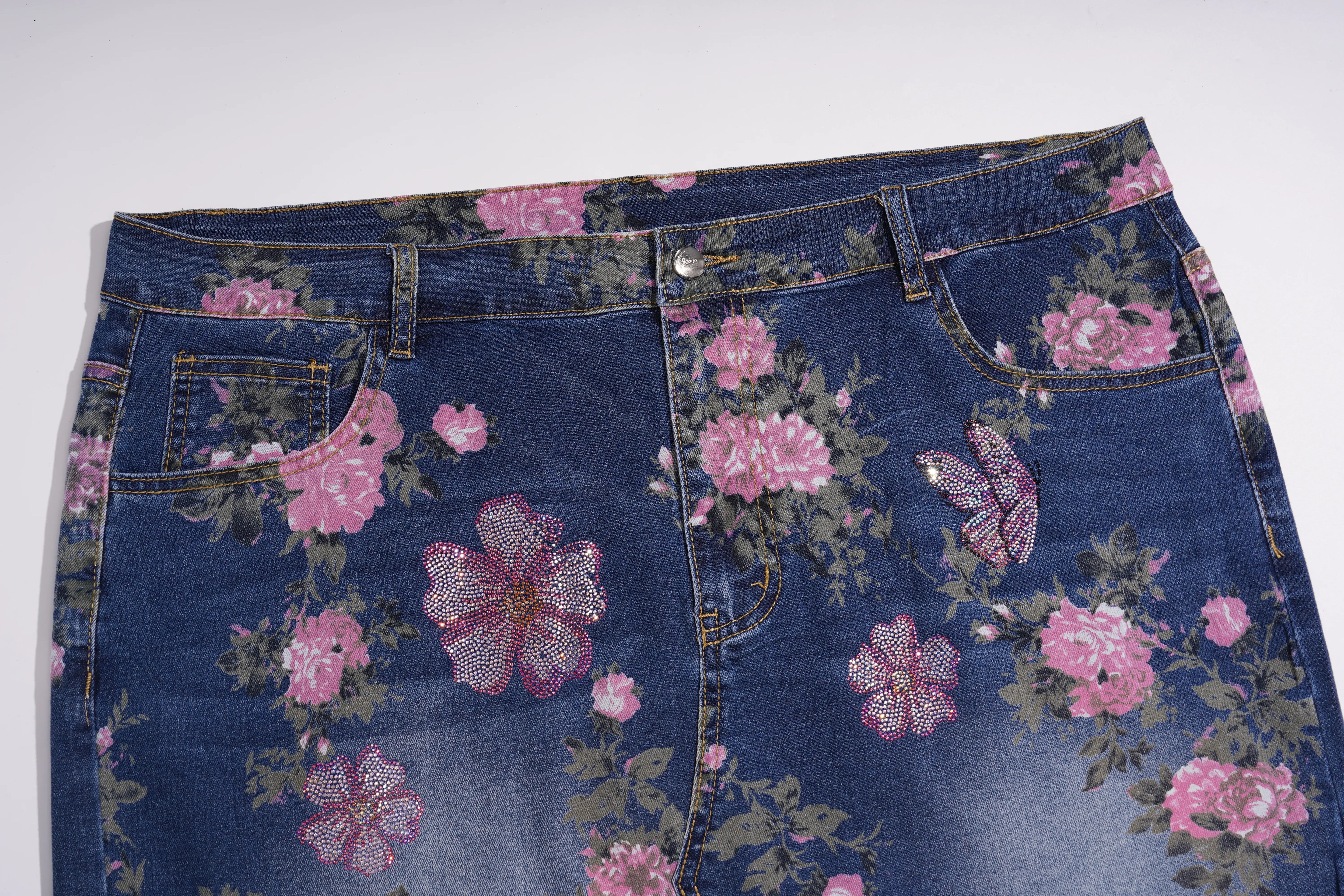 A close-up of a pair of dark blue denim jeans featuring a pink and green floral print with sequined flower embellishments on the front pockets. TCH Floral Butterfly Print Denim Midi Skirt