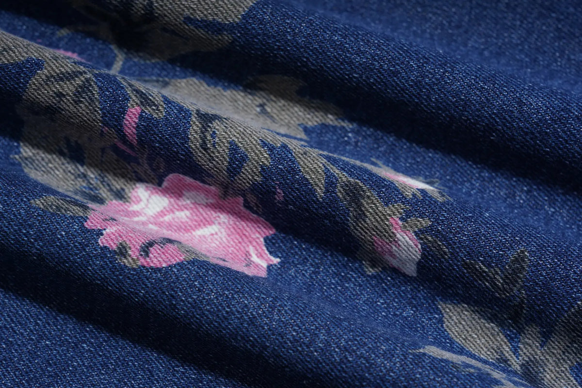 A close-up of a woven fabric with a dark blue base, featuring a pink floral pattern and muted gray-green leaves. TCH Floral Butterfly Rhinestone Wide-Leg Denim Jeans