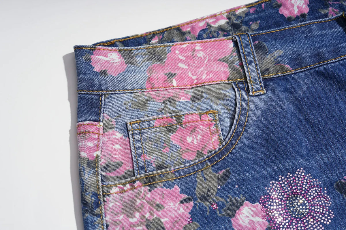 Close-up of a pair of blue denim jeans with a pink floral print, showing the waistband, belt loops, and back pocket. TCH Floral Butterfly Rhinestone Wide-Leg Denim Jeans