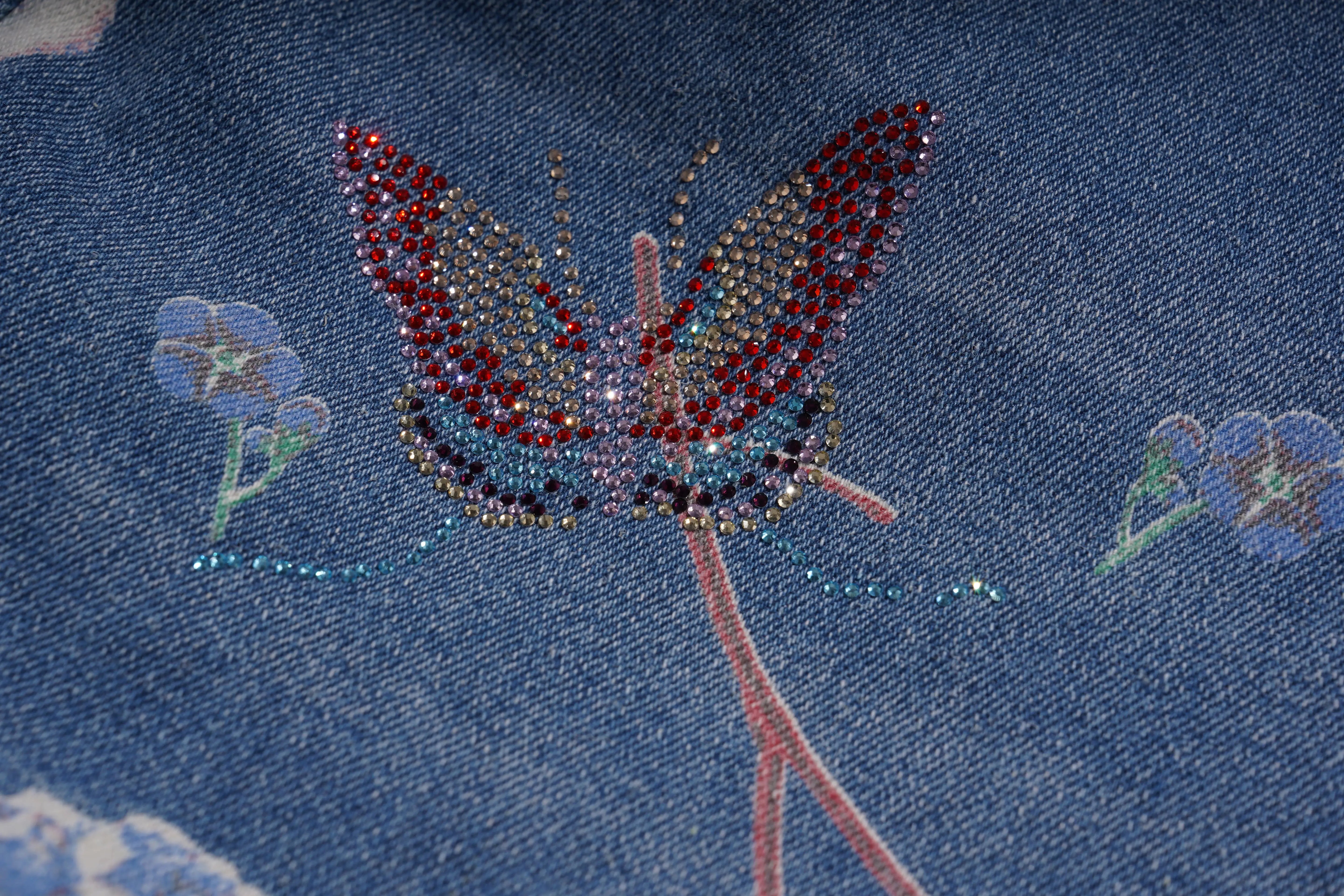 Close-up of a butterfly design with rhinestones on a blue fabric background, TCH Floral Print Rhinestone Butterfly Denim Jeans