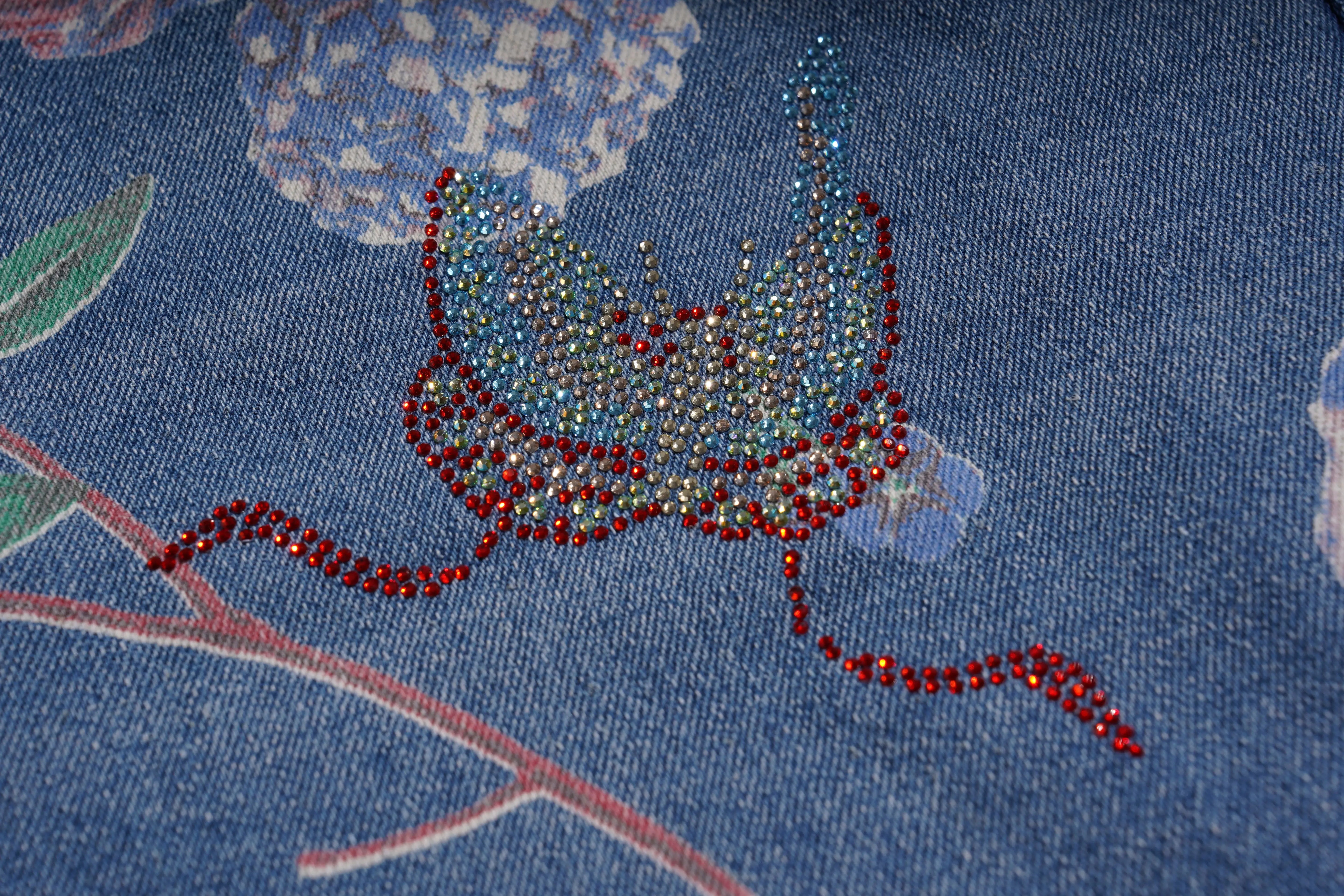 Close-up of a blue fabric with floral patterns and red embellishments. TCH Floral Print Rhinestone Butterfly Denim Jeans