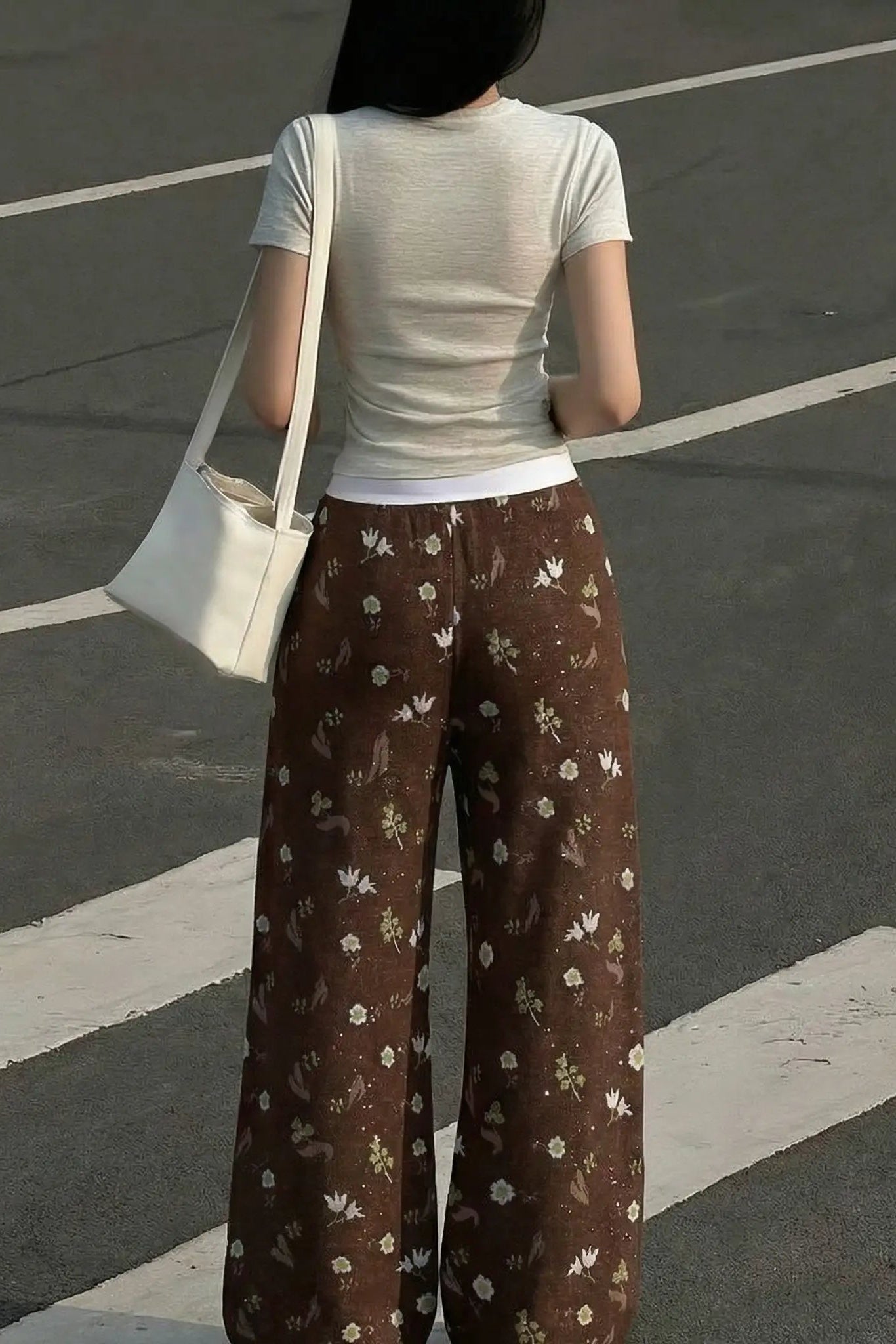 Person wearing a white t-shirt and brown floral pants standing on a road. TCH Floral Rhinestone Accent Sweatpants