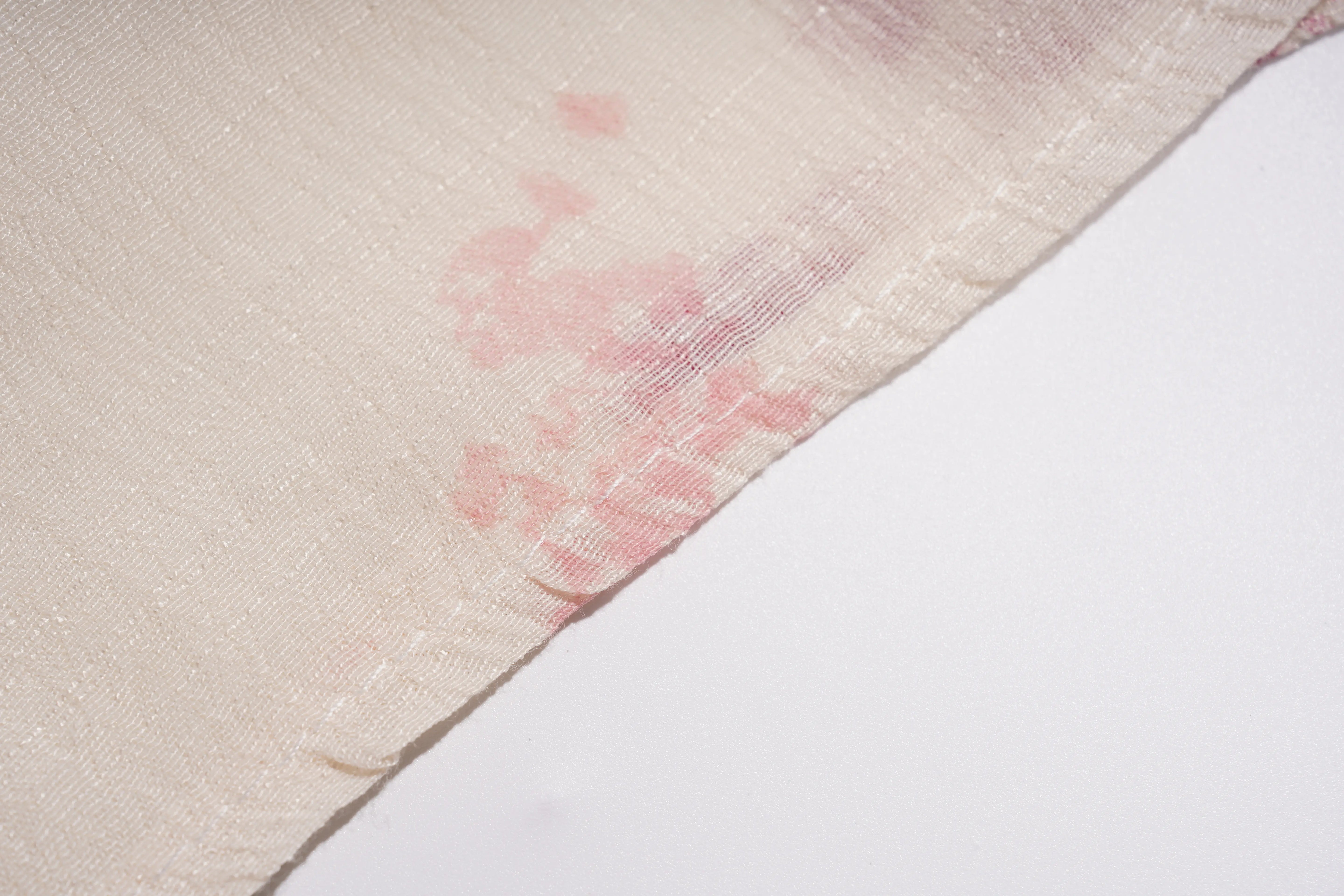 A close-up of a light beige or cream fabric with a subtle pink floral pattern, showing the texture and a stitched edge against a plain white background. TCH Floral Rhinestone Butterfly Print Short Sleeve Blouse