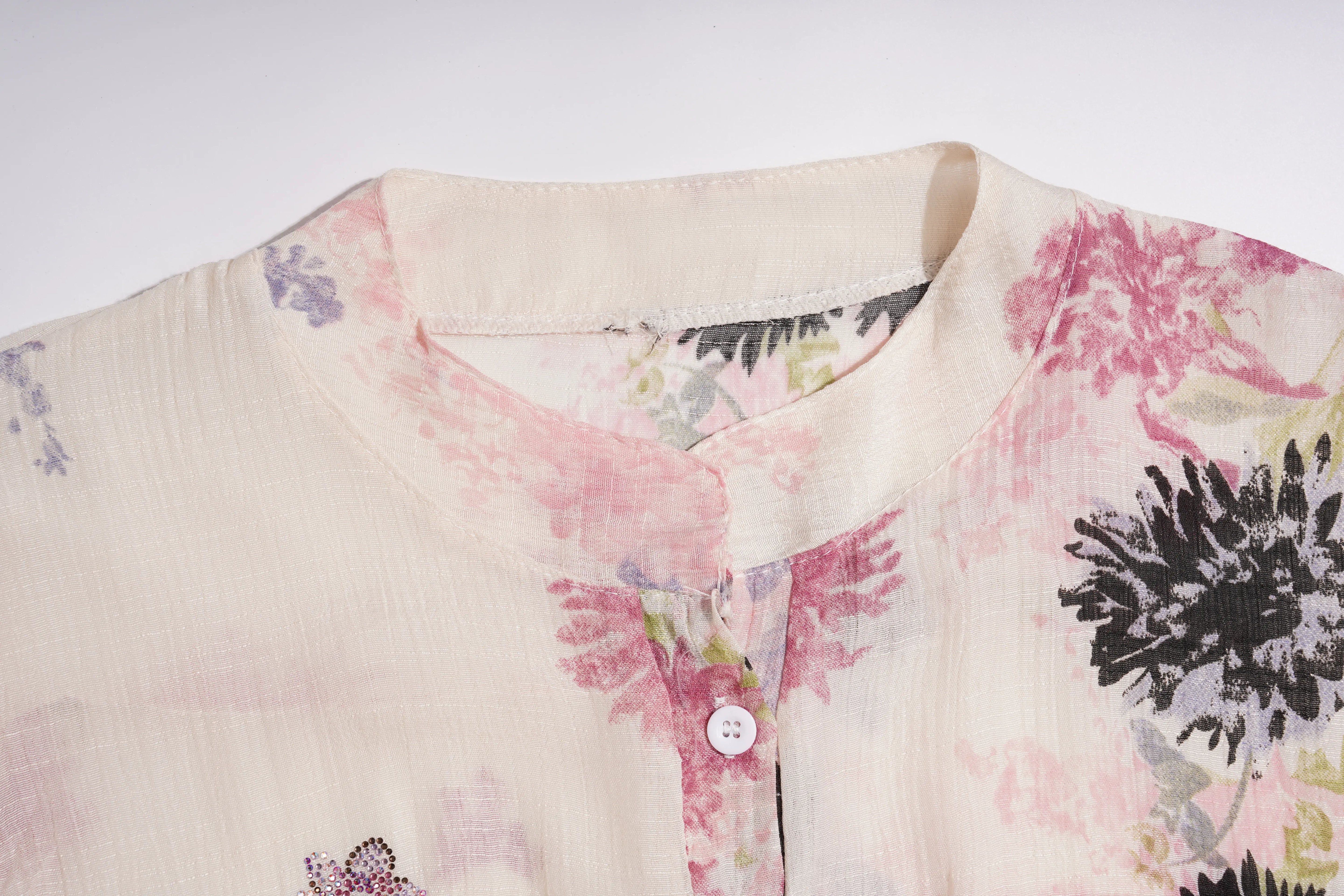Close-up of a cream-colored cotton shirt with a floral print in pink, black, and green, featuring a mandarin collar and a buttoned front. TCH Floral Rhinestone Butterfly Print Short Sleeve Blouse