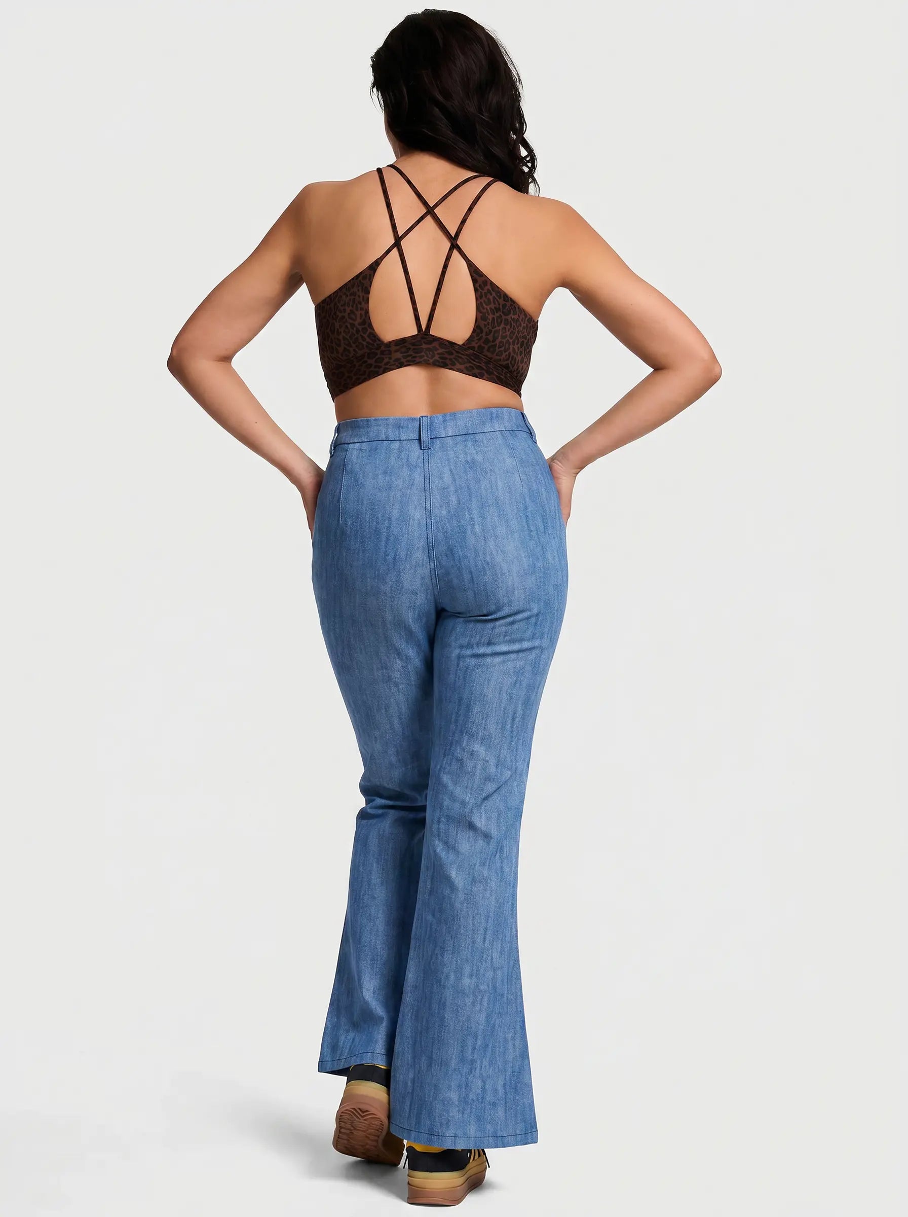 A woman shown from the back wearing a brown lace halter crop top and blue denim flare jeans, standing against a light gray studio background. TCH Floral Rhinestone Wide Leg Denim Jeans