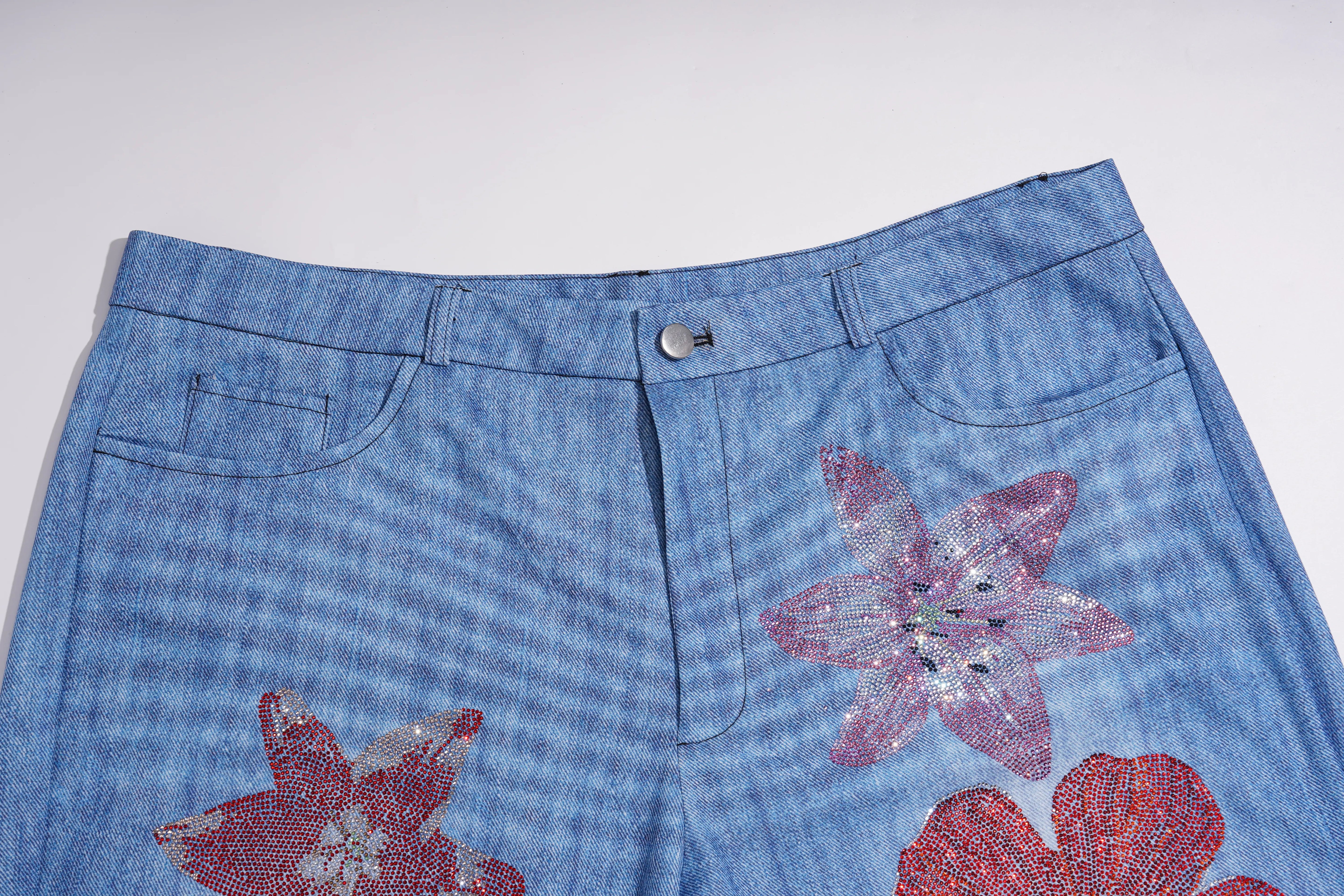 Light blue denim shorts featuring large, textured pink and red sequined flower appliqués on the front, photographed against a plain light gray background. TCH Floral Rhinestone Wide Leg Denim Jeans