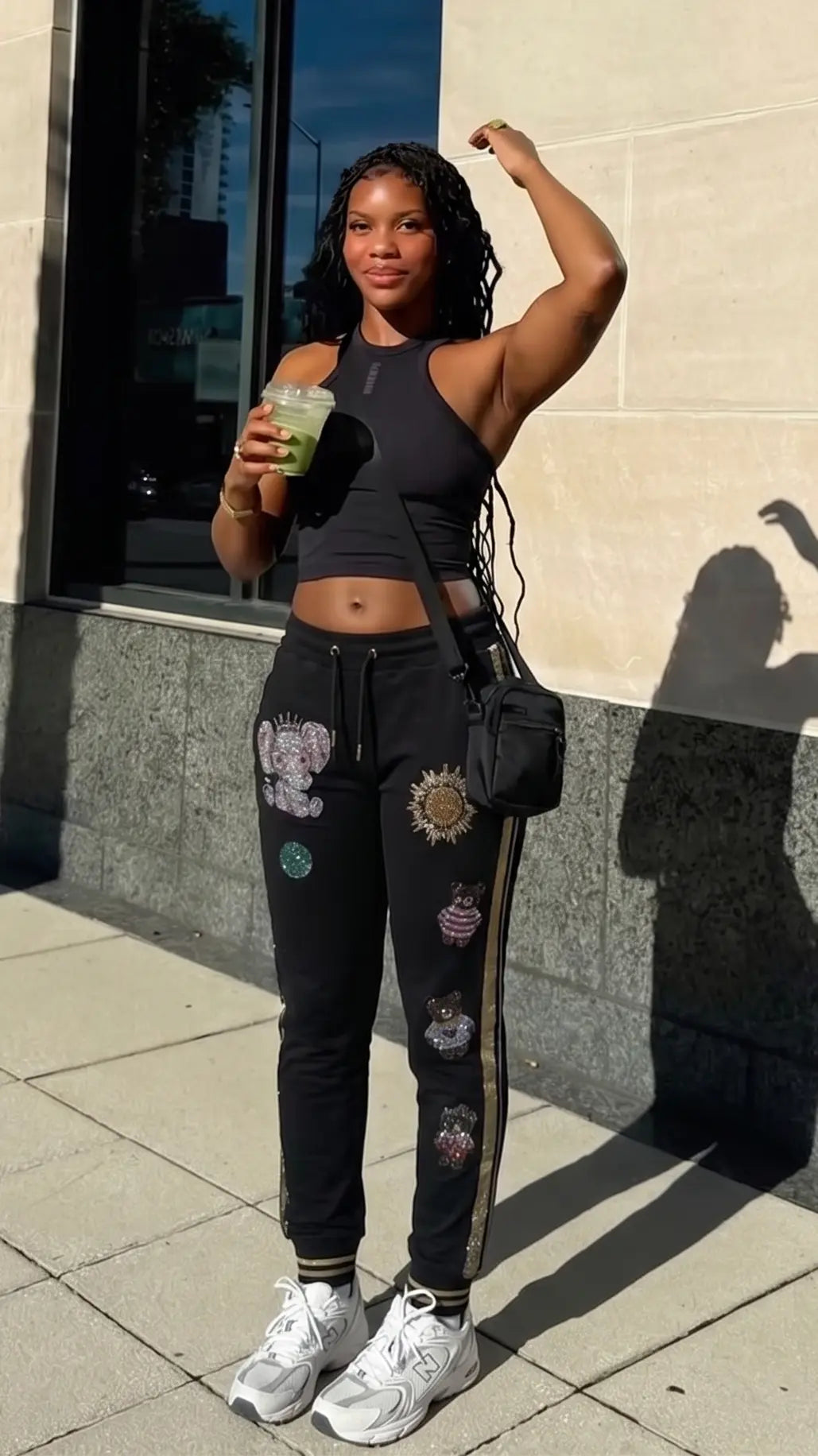 Woman in black athletic wear with colorful designs, holding a drink, standing against a building. TCH Galaxy Rhinestone Black Jogger Pants