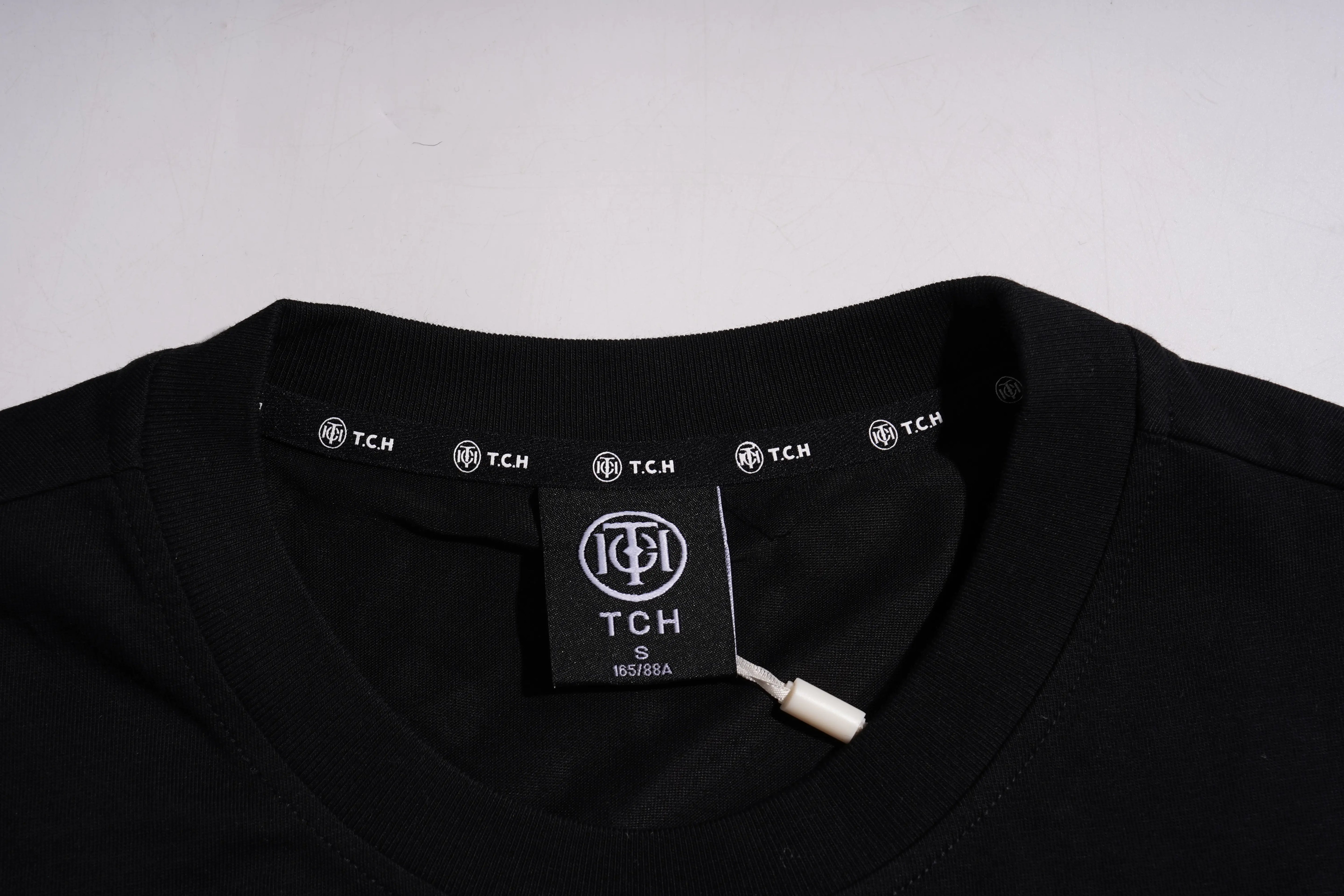 Close-up of a black crewneck t-shirt showing the inner neck label with the TCH logo and brand name. TCH Golden Wing Techno Oversized Graphic T-Shirt