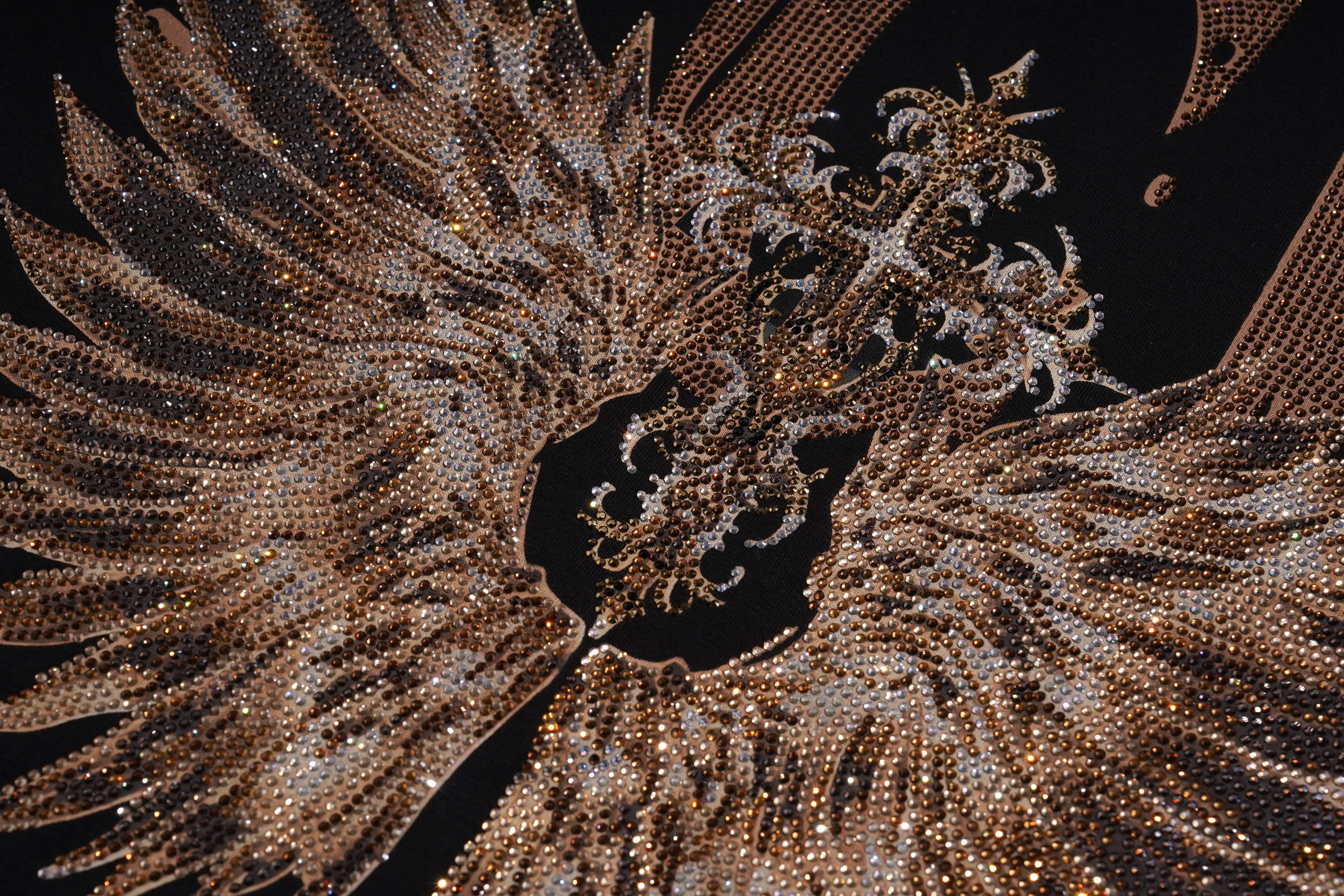 A close-up of an ornate, highly textured feather-like embellishment or decorative panel made of dense metallic gold and silver rhinestones, set against a solid black background. TCH Golden Wing Techno Oversized Graphic T-Shirt