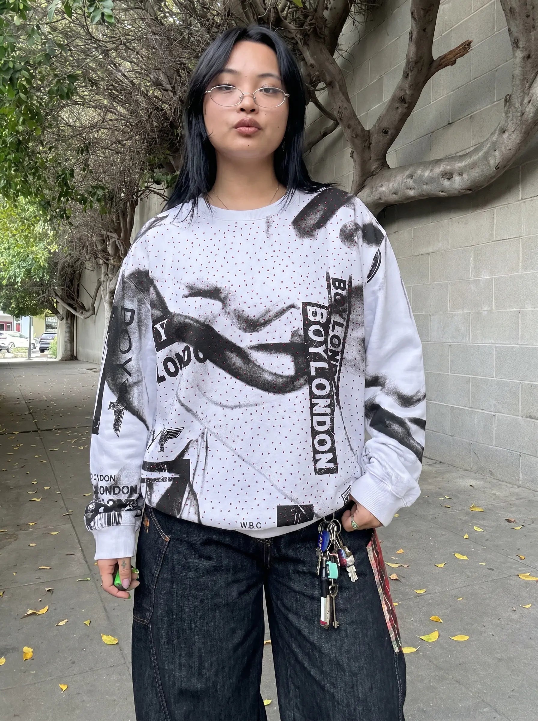 Person wearing a white sweatshirt with black text and graphics, standing outdoors.TCH Graffiti Logo Print Crewneck Sweatshirt