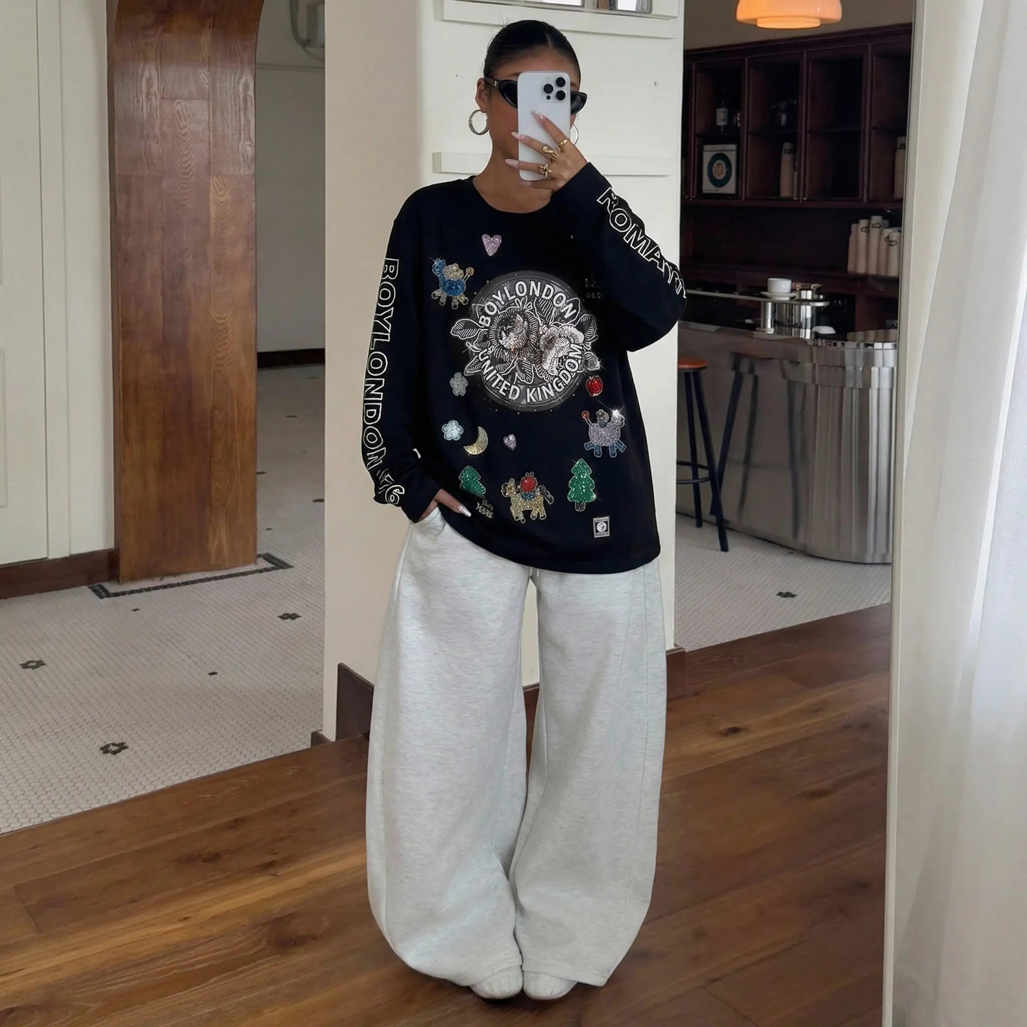 Person wearing a black sweater with colorful designs and white pants in a room. TCH Graphic Rhinestone Heat Transfer Crewneck Sweatshirt-