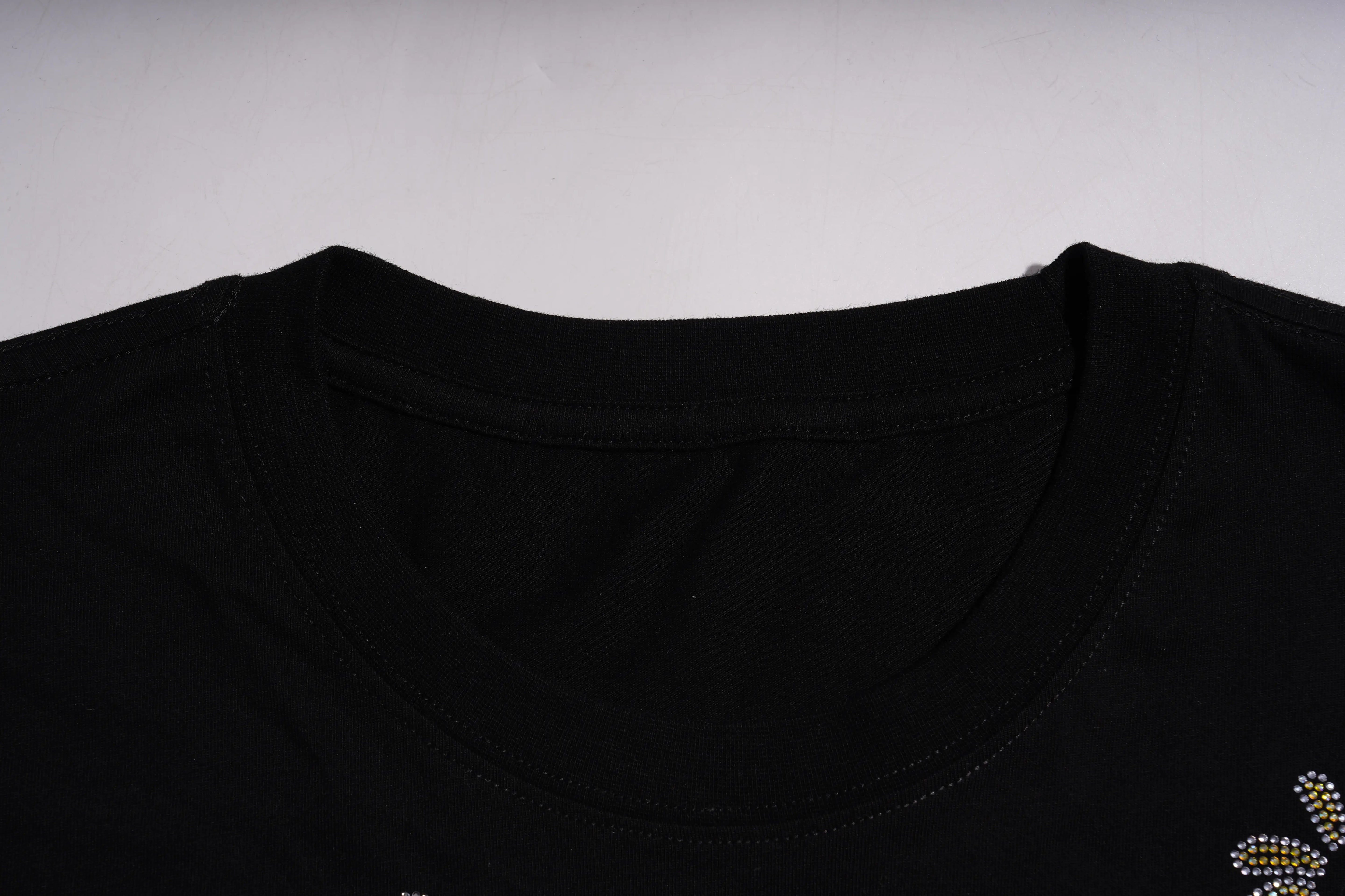 Close-up of a black shirt with a small floral embellishment on a light gray background TCH Graphic Rhinestone Heat Transfer Crewneck Sweatshirt-