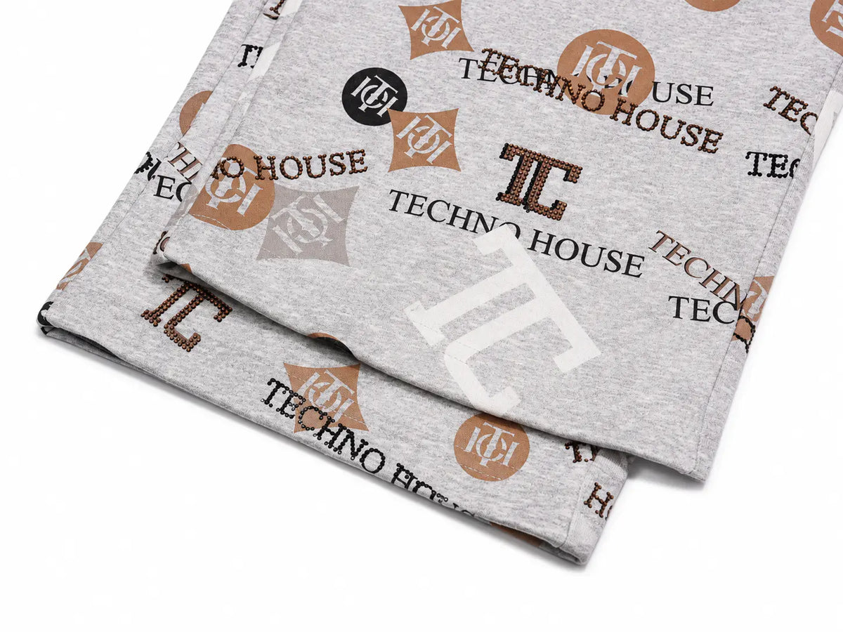 A folded light gray heather sweatshirt featuring an all-over repeating 'Techno House' logo print in brown, black, and white, displayed on a clean white background. TCH Gray Techno Graphic Wide-Leg Sweatpants