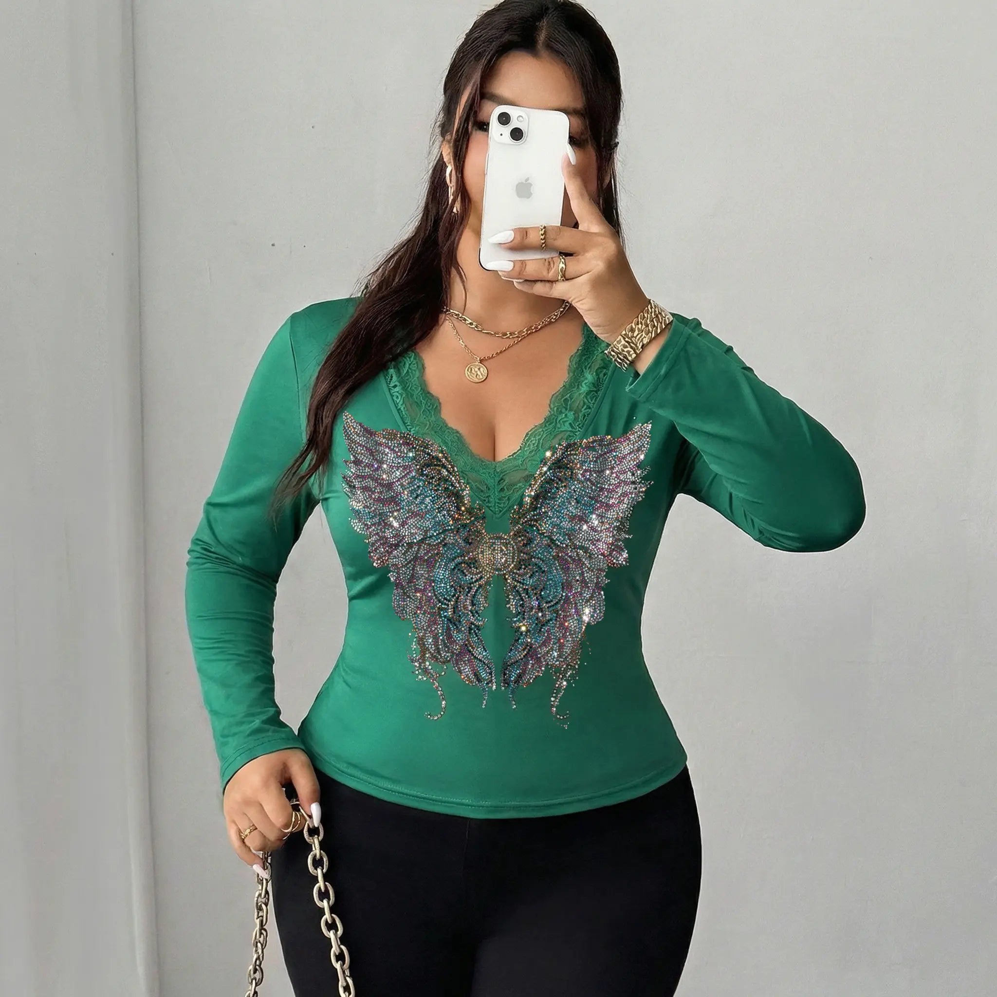 Woman wearing a green long-sleeve top with a butterfly design, taking a mirror selfie. TCH Green Lace Trim V-Neck Rhinestone Wing Long Sleeve Top