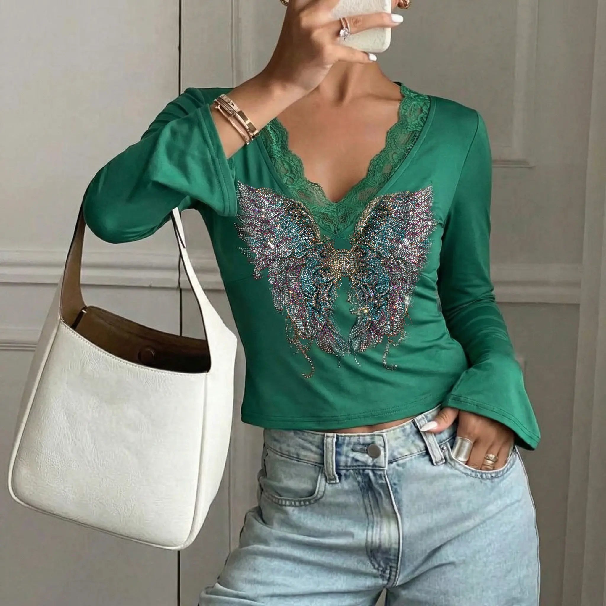 Person wearing a green top with a butterfly design and holding a white handbag. TCH Green Lace Trim V-Neck Rhinestone Wing Long Sleeve Top