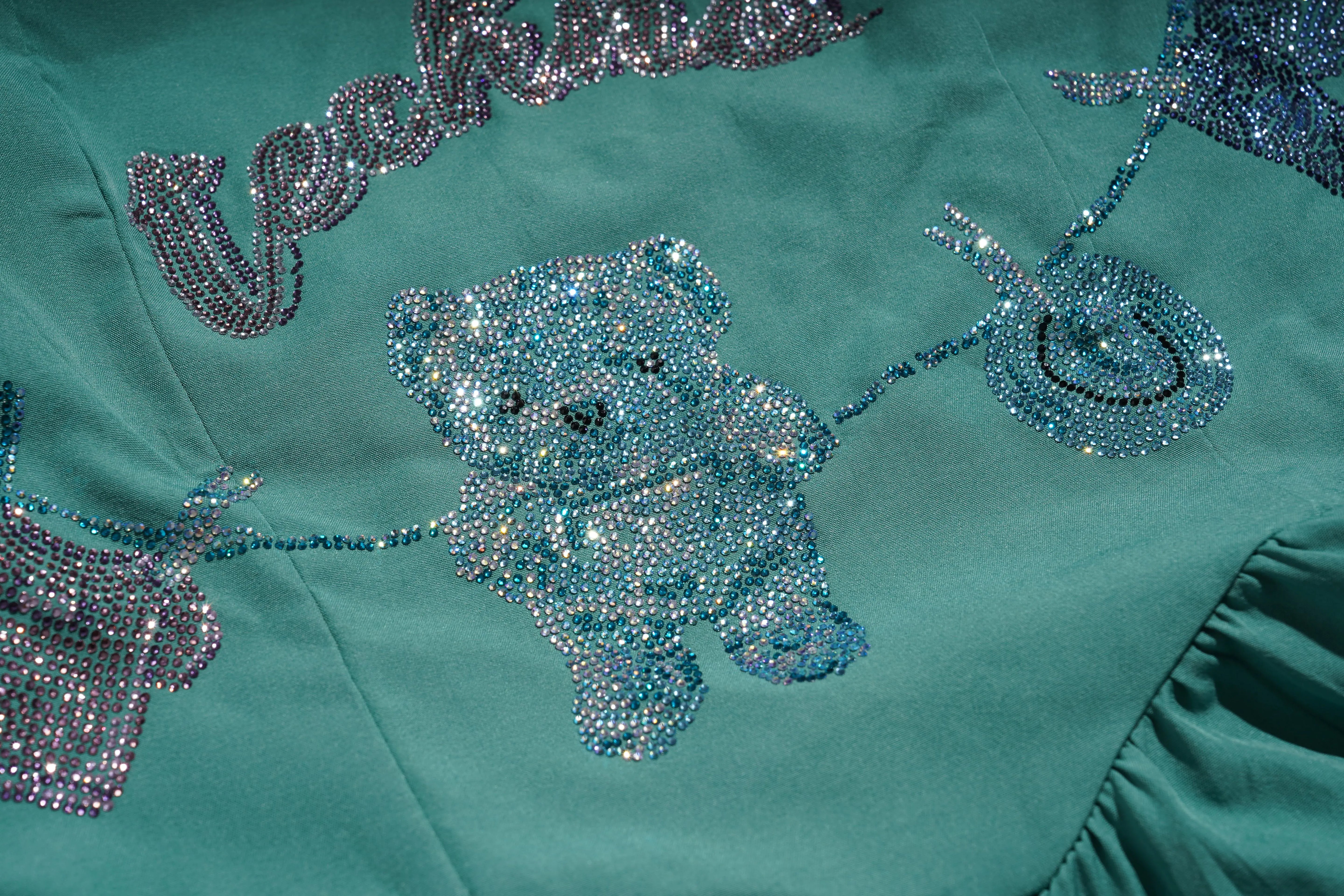 Teal fabric with a teddy bear and bicycle design made of sequins on a teal background. TCH Green Rhinestone Teddy Laundry Story Dress