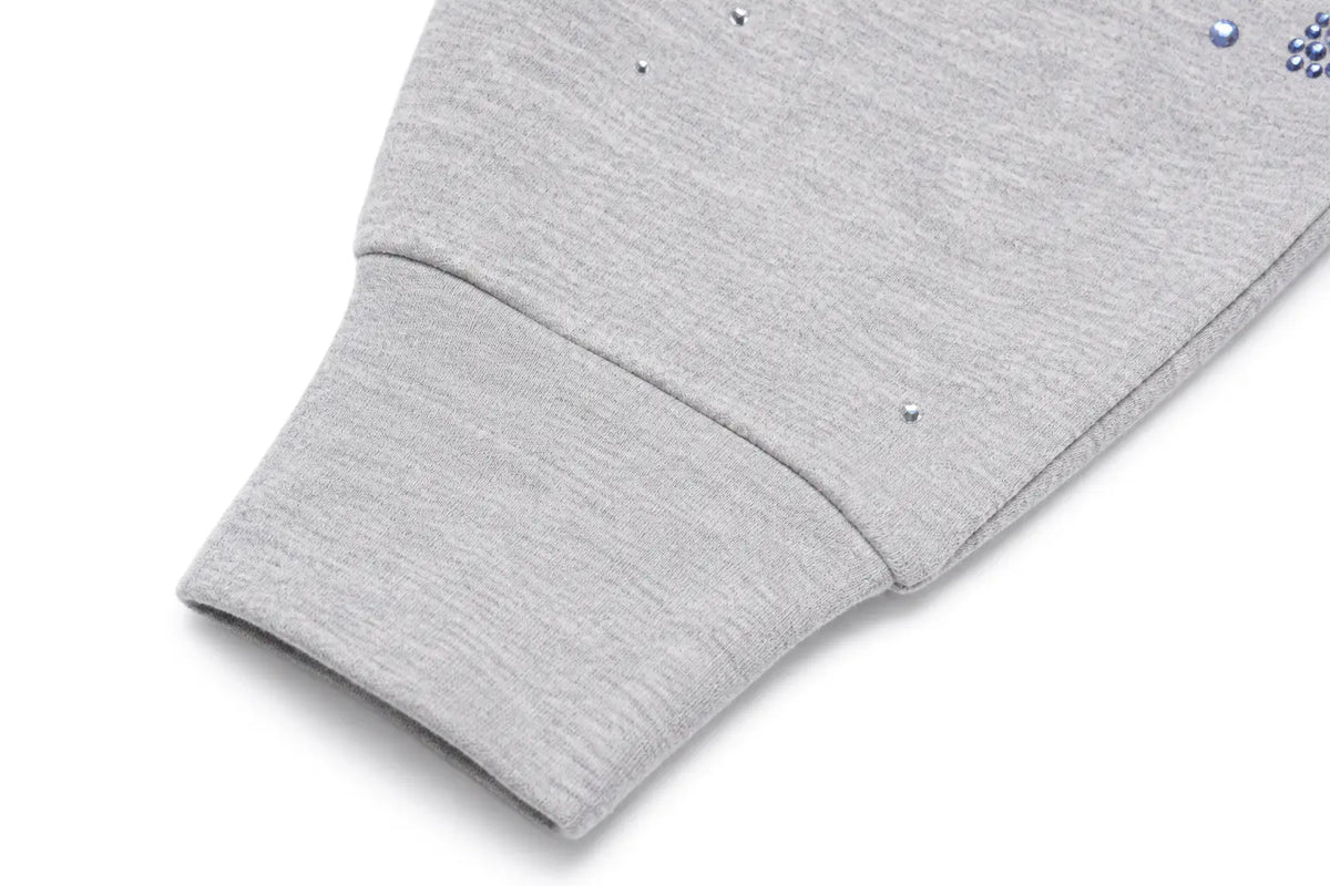 Close-up of a light gray heather sweatshirt sleeve with a ribbed cuff and small rhinestone embellishments on the fabric, shown on a white background. TCH Grey Angel Wing Zip Up Hoodie
