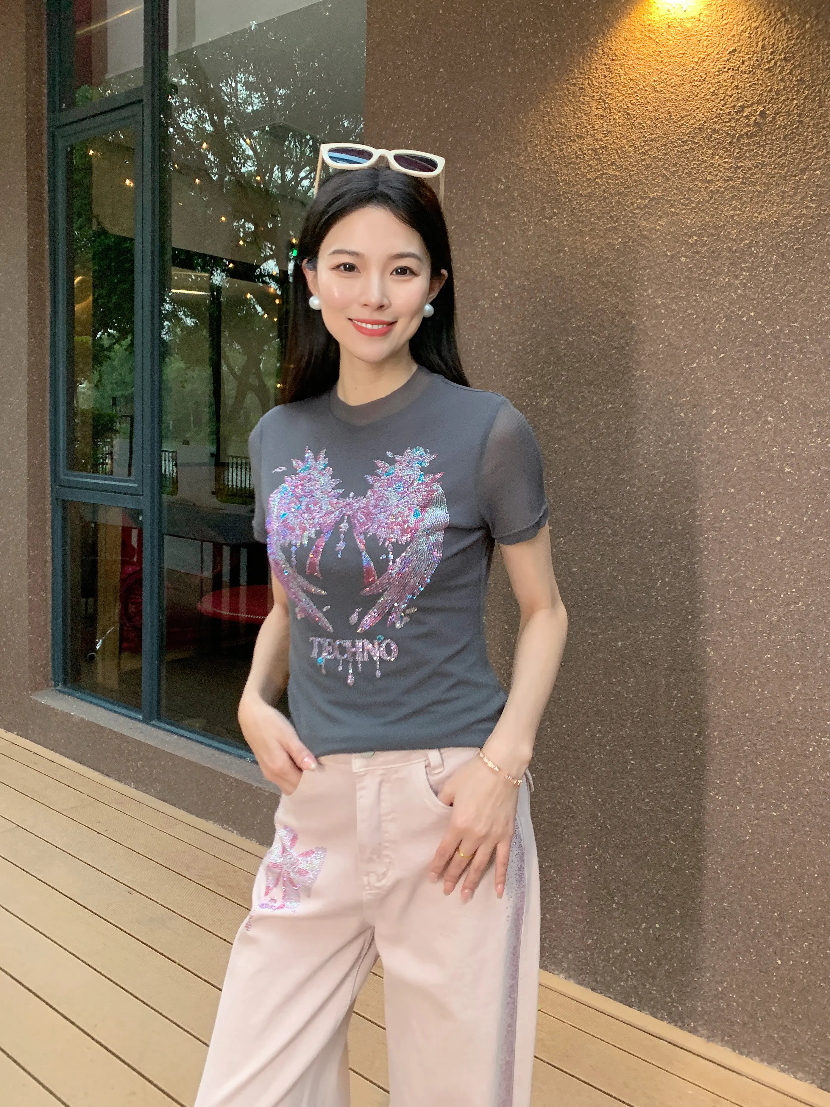 Woman wearing a graphic t-shirt and light pants standing outside a building. TCH Grey Rhinestone Pink Wings Graphic T-Shirt
