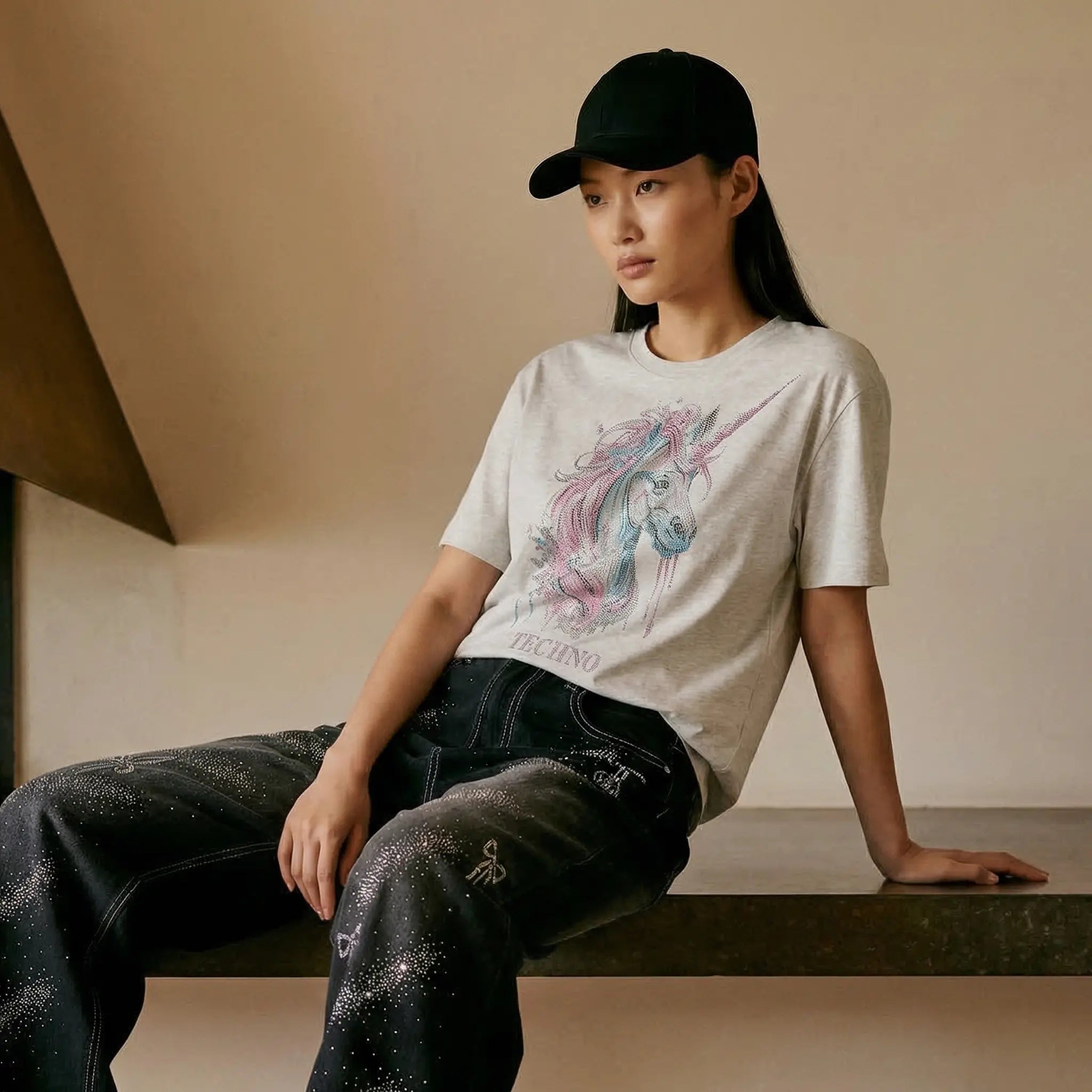 Person wearing a graphic t-shirt and black cap sitting on a bench. TCH Grey Rhinestone Unicorn Graphic T-Shirt