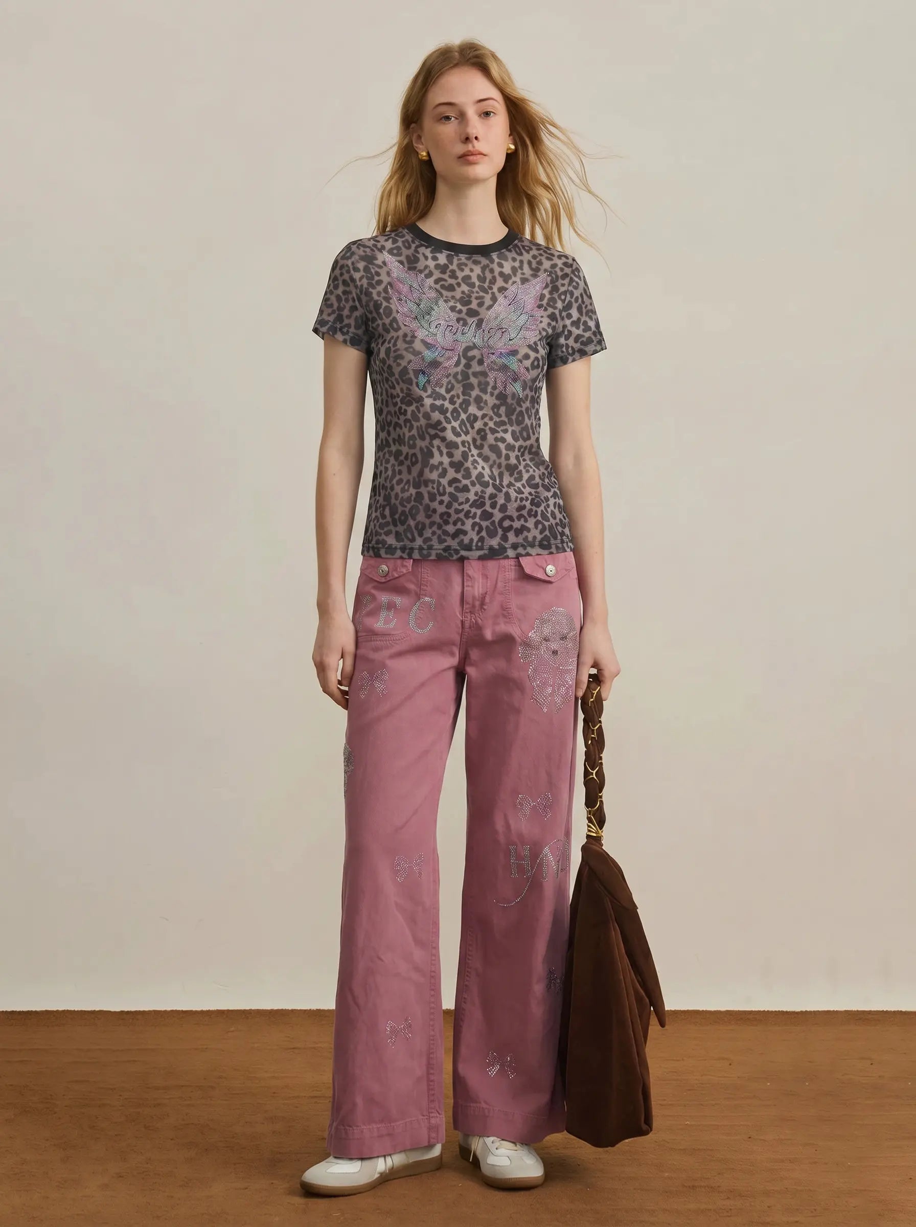 Woman wearing a patterned top and pink pants holding a brown jacket against a neutral background, TCH Leopard Print Rhinestone Butterfly Fitted T-Shirt